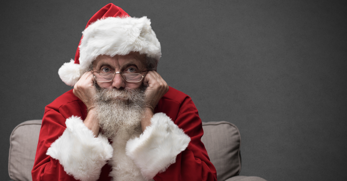 Pensive-looking Santa Claus resting his chin on his hands and looking directly at the camera.