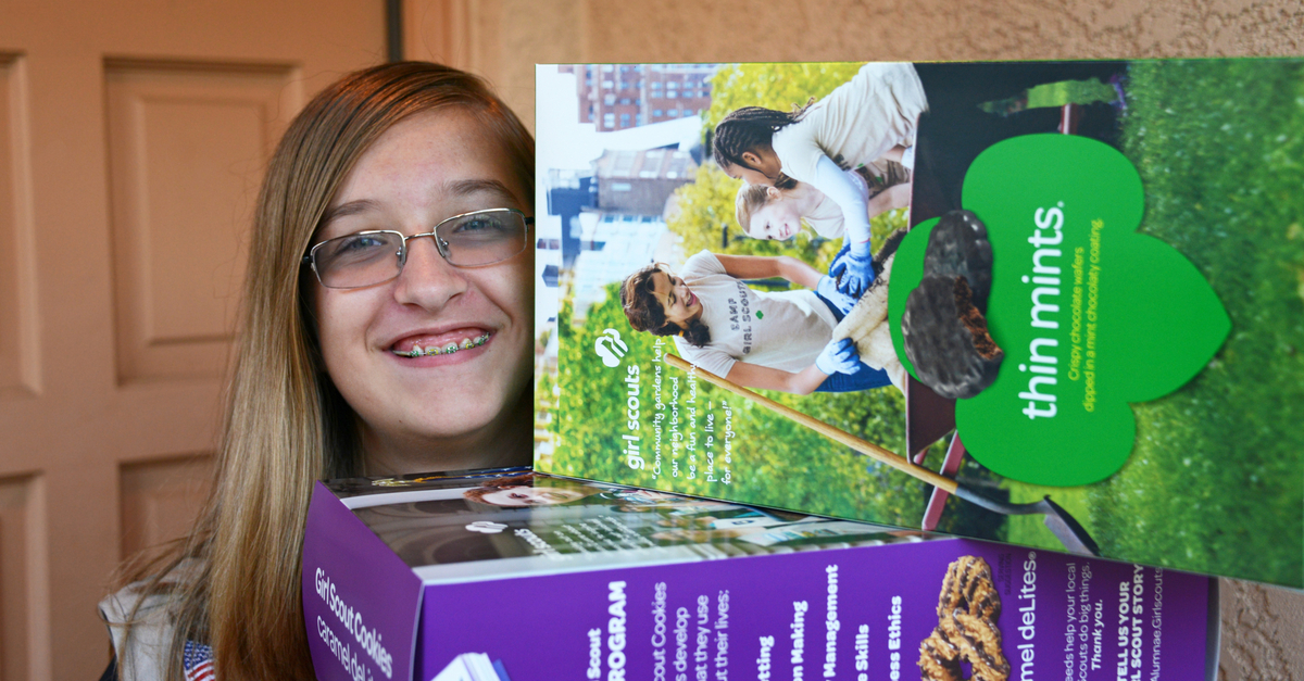 Smiling Girl Scout at door with boxes of cookies