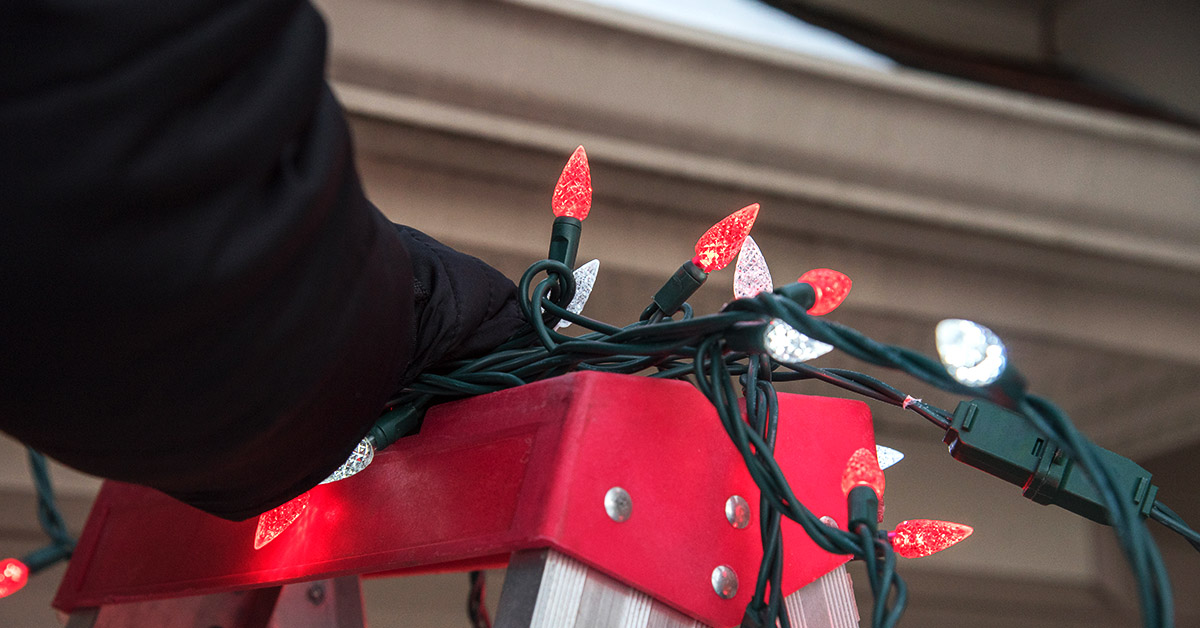 Person standing on ladder to hang Christmas lights