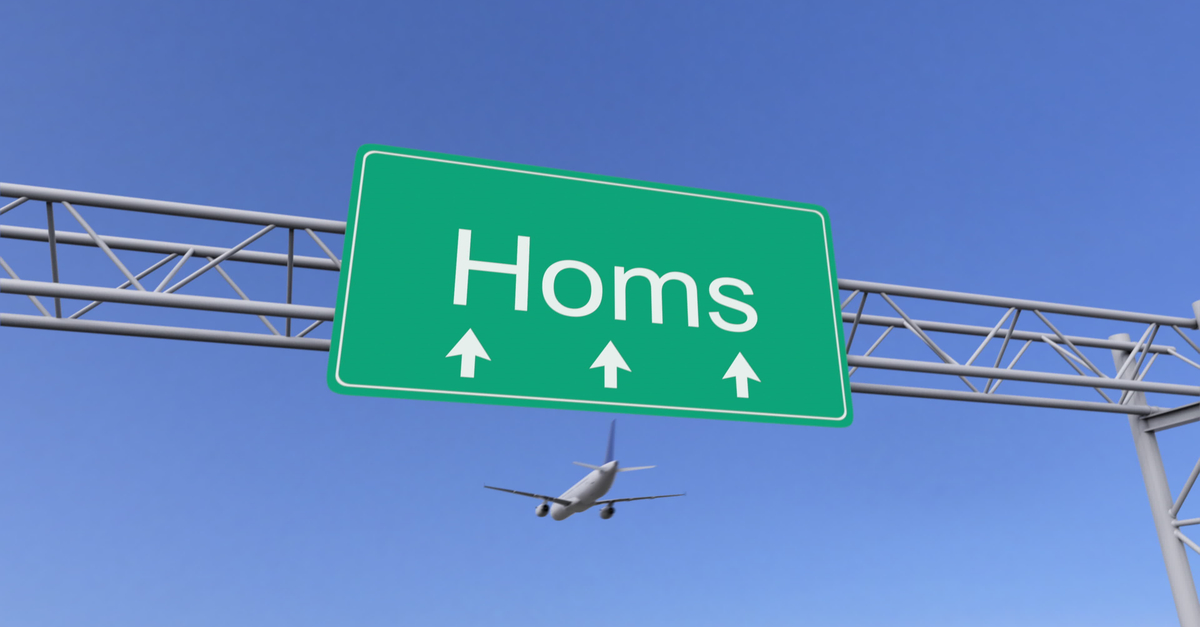 Airplane passing above a sign that reads "Homs"