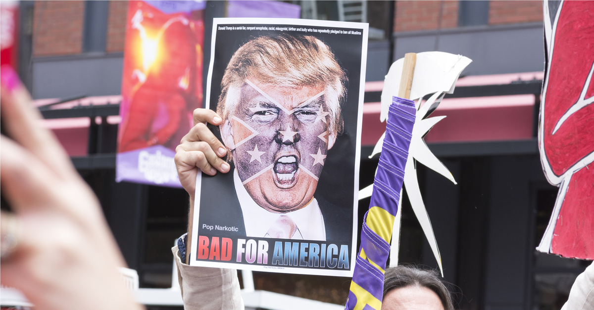 A protester holds a sign featuring an angry photo of Donald Trump and reading "Bad for America" at an anti-Trump protest outside a Trump rally in San Diego.