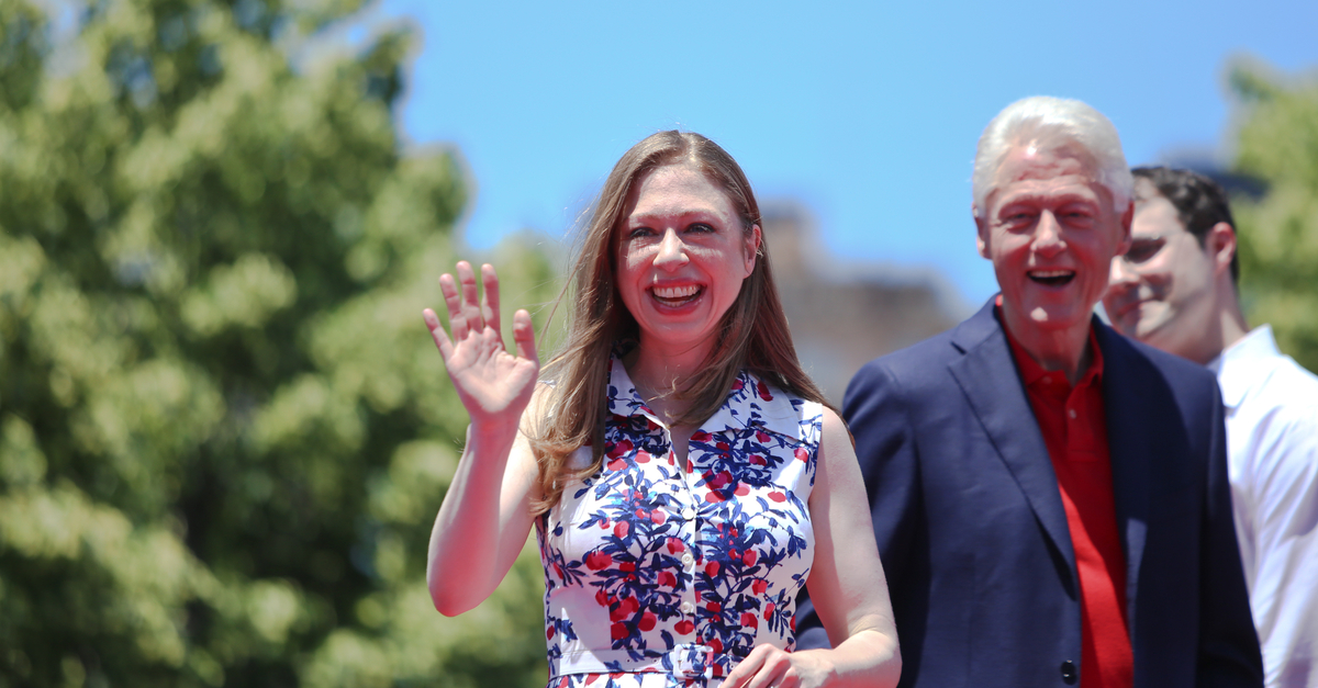 Chelsea Clinton waving at the camera with her father, Bill Clinton, in the background