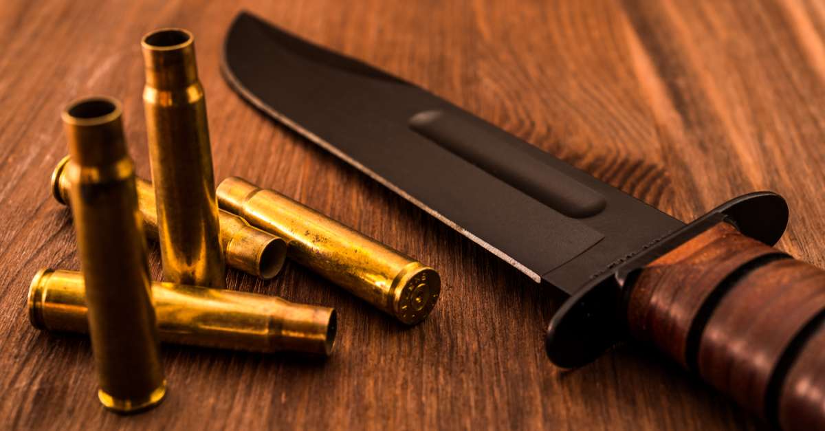 Empty shells, a rifle, and combat knife on a wooden table