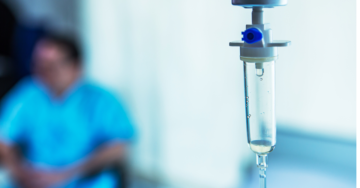 Intravenous bag with patient in background in hospital room