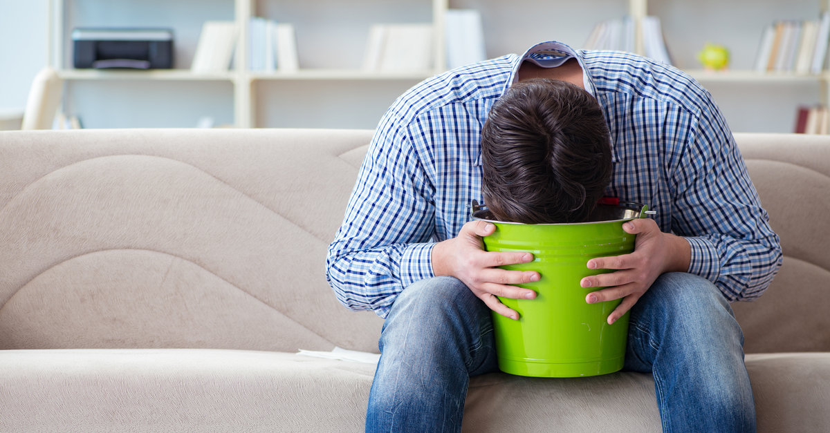 Person sitting on a couch vomiting into a bucket
