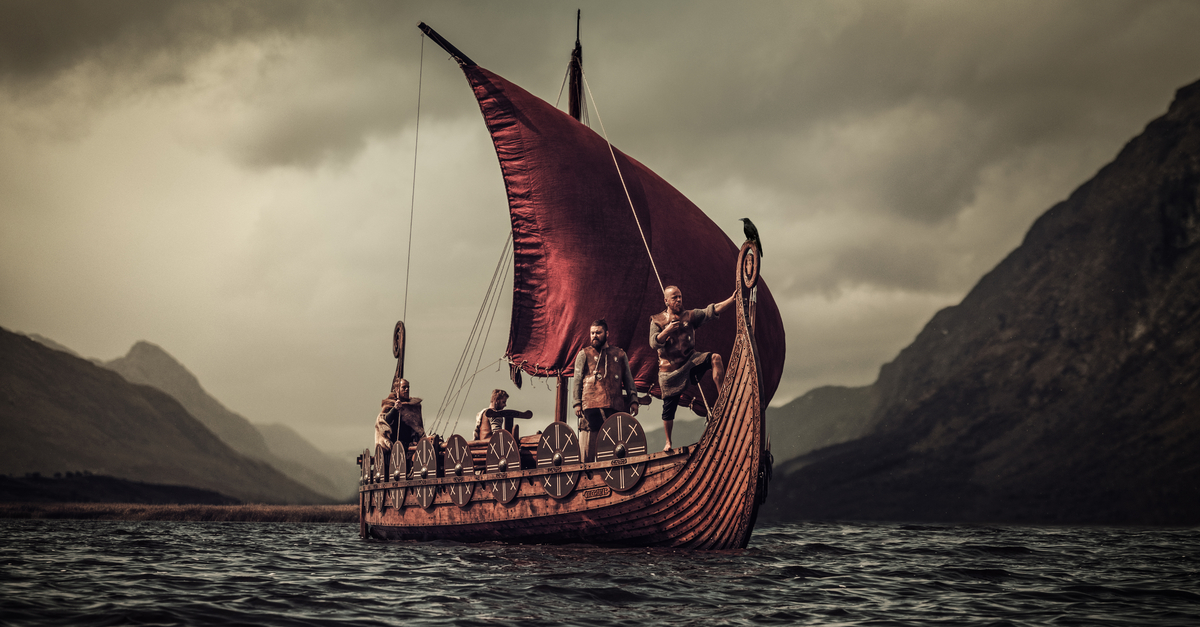 A group of Vikings floating on the sea on Drakkar with mountains on the background.