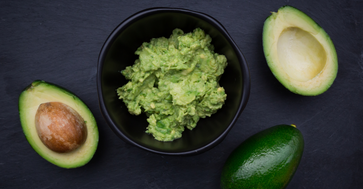 Bowl of guacamole surrounded by avocados.