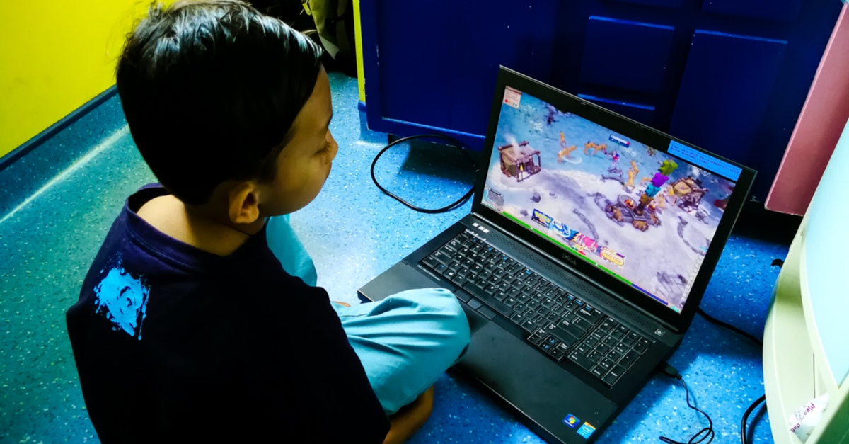 A child sitting on a floor watching a YouTube channel on a laptop.
