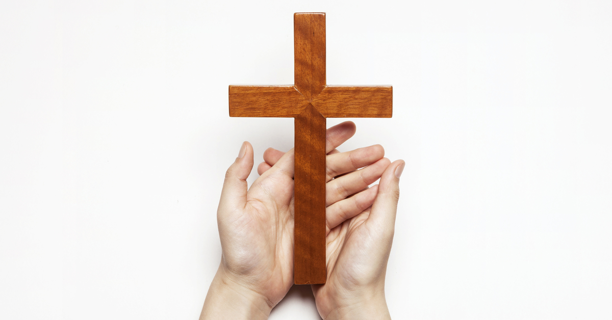 Hands holding a wooden crucifix against a plain white background.