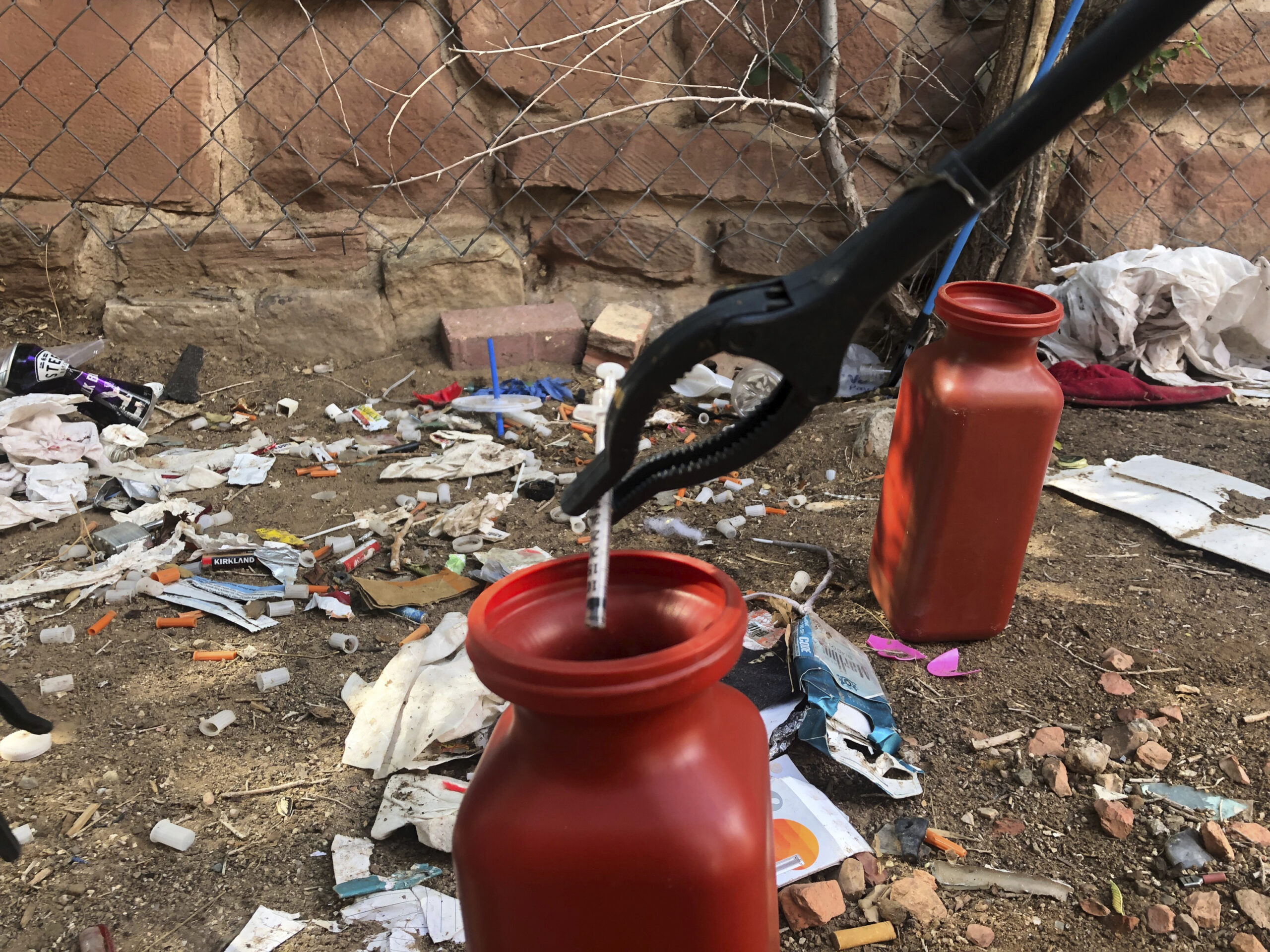 FILE - In this Aug. 9, 2019, file photo, a drug syringe found behind a vacant property in northeast Albuquerque, N.M., is placed into a container, as crews attempt to clear the lot of needles and other heroin paraphernalia. In what would be a first in the U.S., possession of small amounts of heroin, cocaine, LSD and other hard drugs would be decriminalized in Oregon under a ballot measure that voters are deciding on in Tuesday's election. Instead of going to trial and facing possible jail time, a person would have the option of paying a $100 fine or attend new "addiction recovery centers." (AP Photo/Mary Hudetz, File)