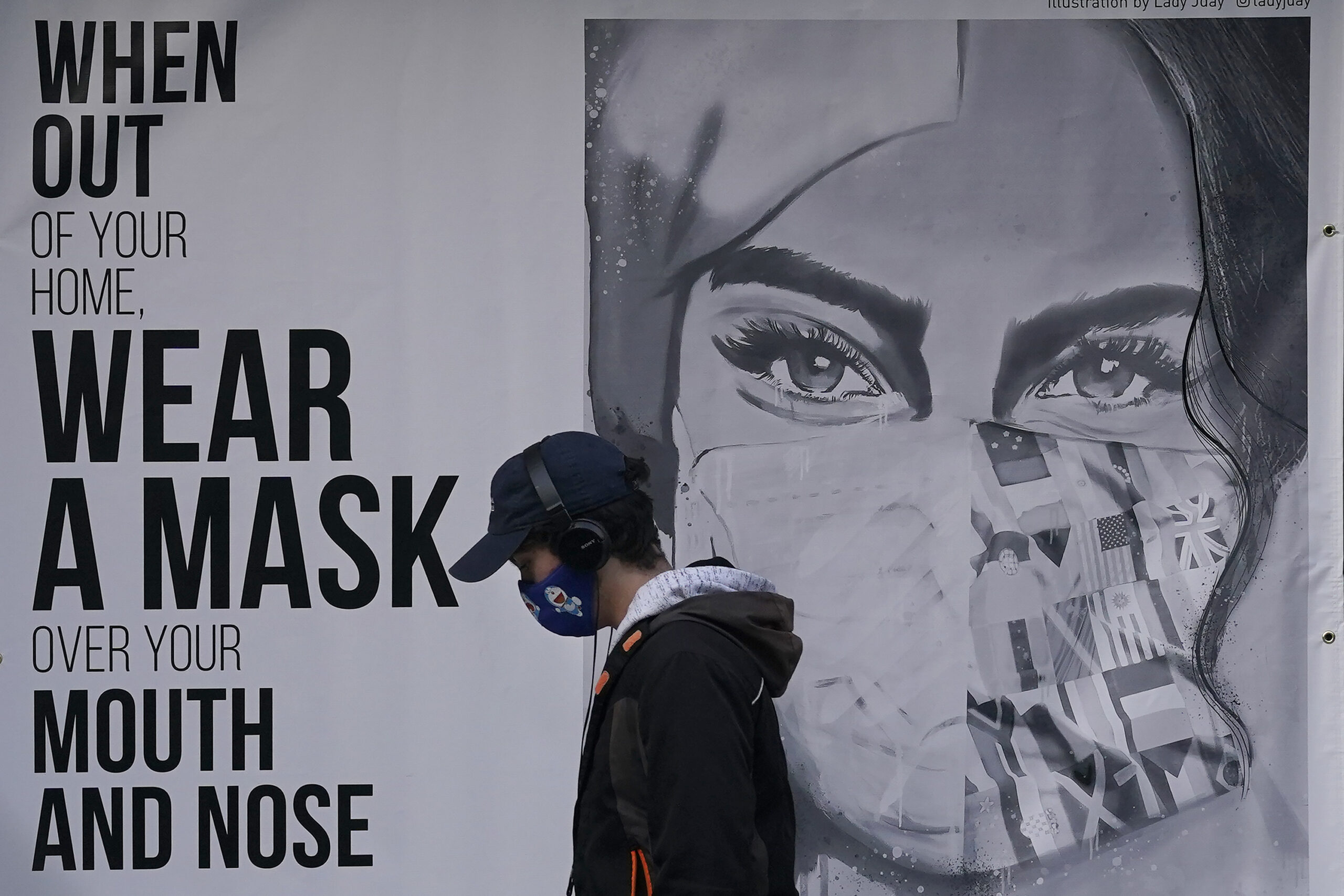 FILE - In this Nov. 21, 2020, file photo, a pedestrian walks past a mural reading: "When out of your home, Wear a mask over your mouth and nose," during the coronavirus outbreak in San Francisco. From speculation that the coronavirus was created in a lab to a number of hoax cures, an overwhelming amount of false information about COVID-19 has followed the virus as it circled the globe over the past year. (AP Photo/Jeff Chiu, File)