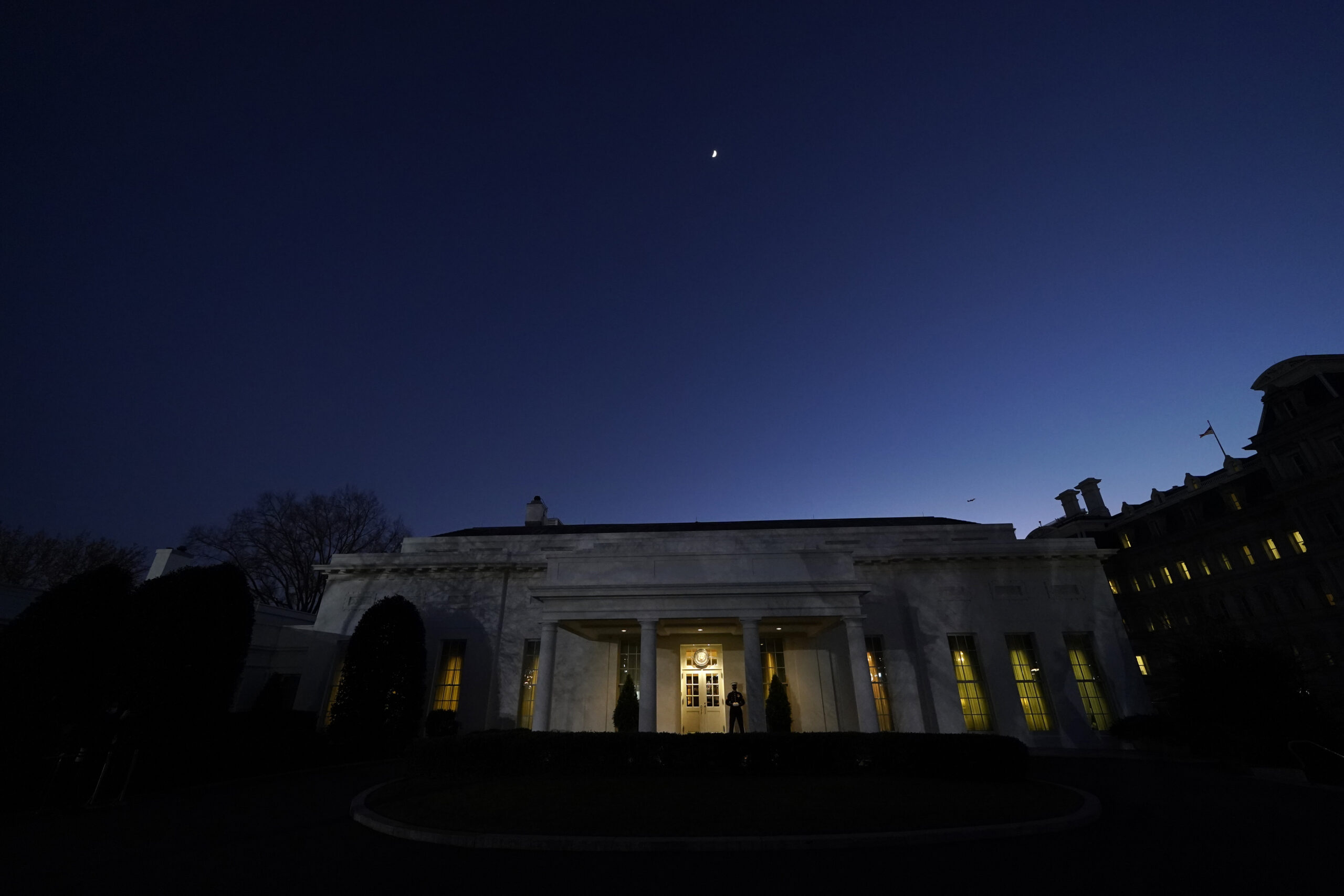 The moon rises over the West Wing of the White House, on President Donald Trump's last day in office, Tuesday, Jan. 19, 2021, in Washington. The Marine guard at the entrance signifies the president is in the Oval Office. (AP Photo/Gerald Herbert)