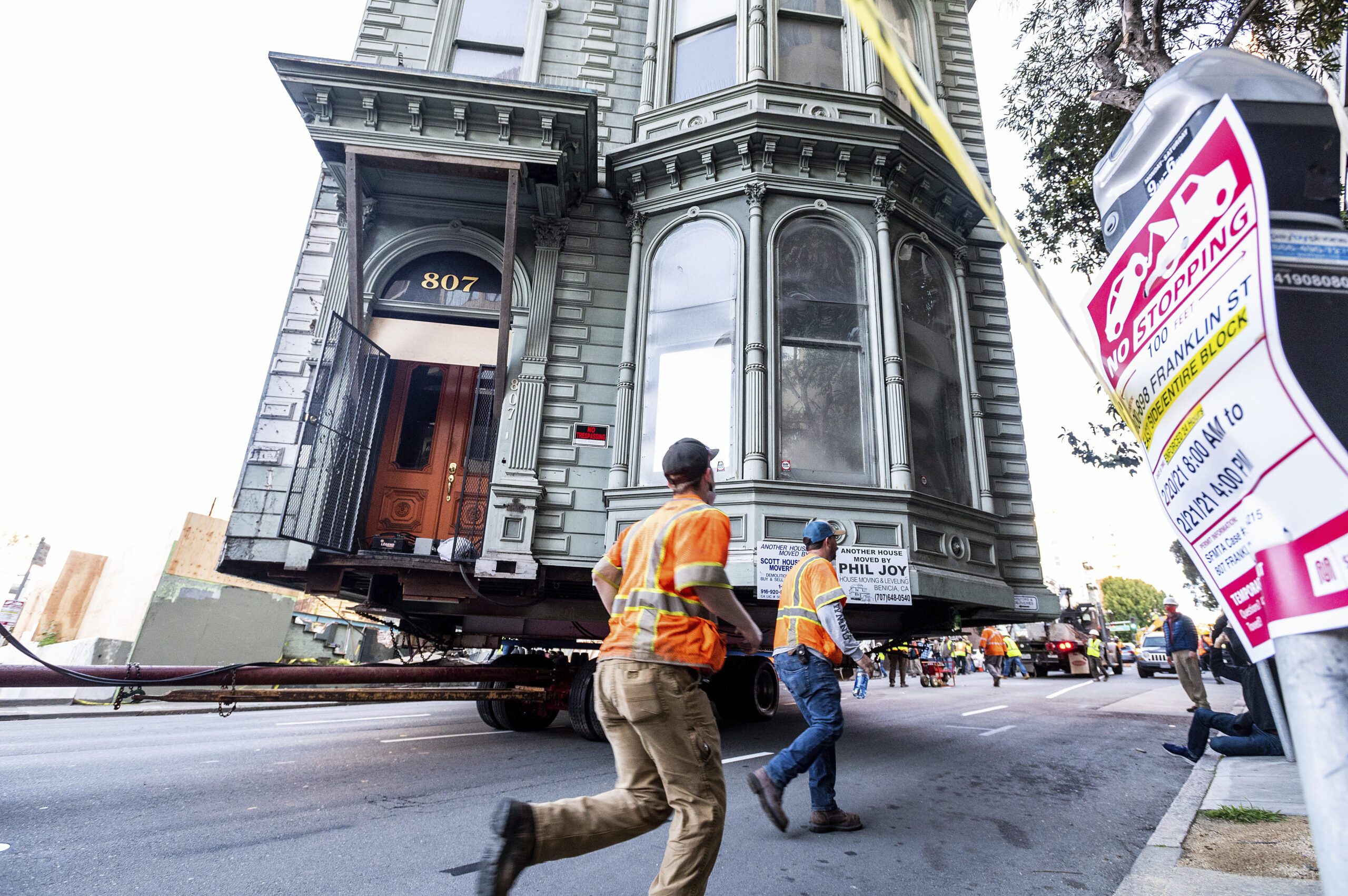 CORRECTS APPROXIMATE COST TO $400,000, INTEAD OF $200,000 - Workers pass a Victorian home as a truck pulls it through San Francisco on Sunday, Feb. 21, 2021. The house, built in 1882, was moved to a new location about six blocks away to make room for a condominium development. According to the consultant overseeing the project, the move cost approximately $400,000 and involved removing street lights, parking meters, and utility lines. (AP Photo/Noah Berger)