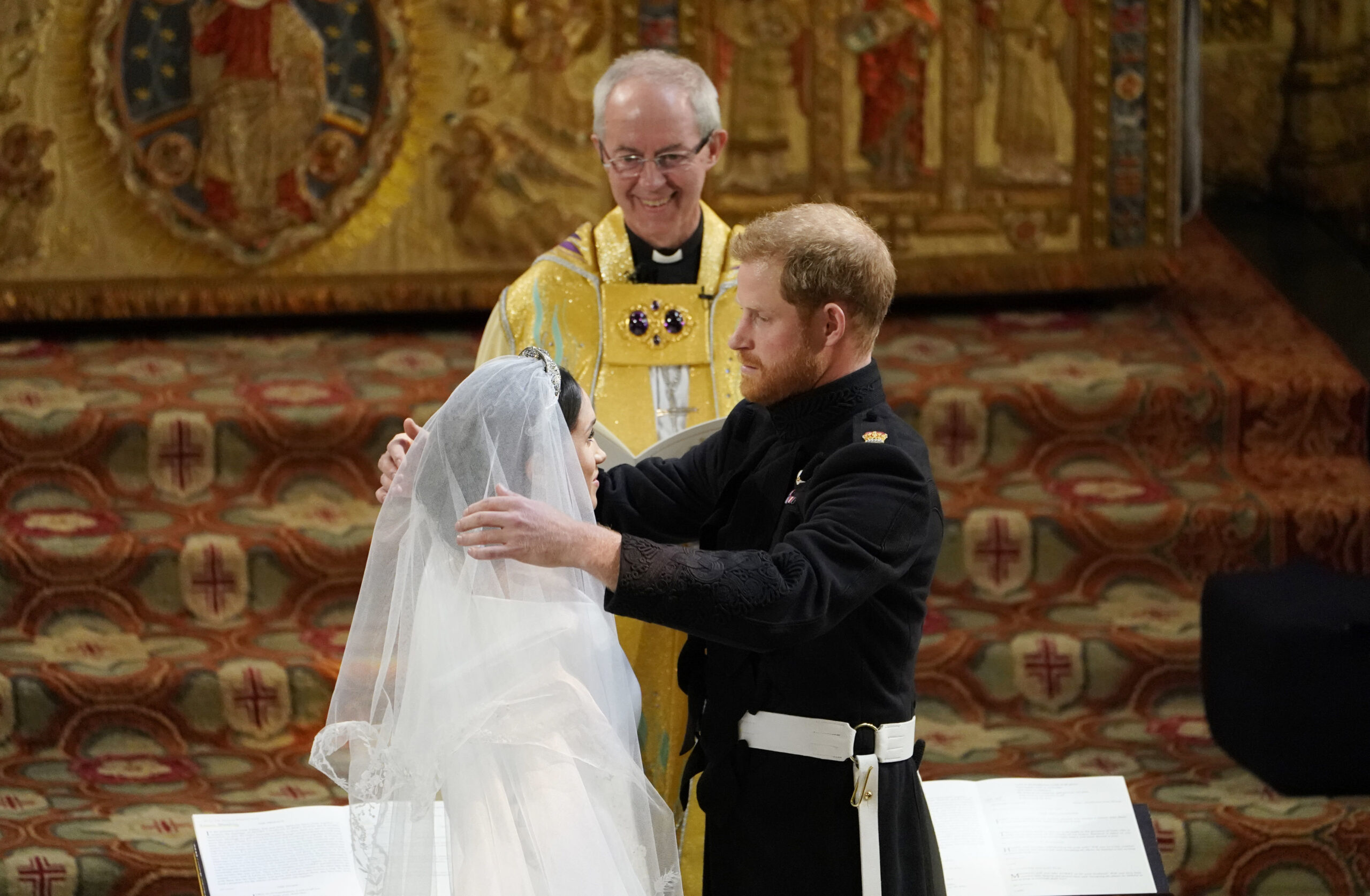 FILE - In this Saturday, May 19, 2018 file photo, Britain's Prince Harry pulls back the veil of Meghan Markle watched by Archbishop of Canterbury Justin Welby during their wedding at St. George's Chapel in Windsor Castle in Windsor, near London, England. The archbishop of Canterbury has confirmed that he married Prince Harry and Meghan Markle at Windsor Castle in May 2018, despite the couple’s claim they had another, private, ceremony three days earlier. During an interview with Oprah Winfrey earlier this month, Meghan said that “three days before our wedding we got married.” (Owen Humphreys/pool photo via AP, File)