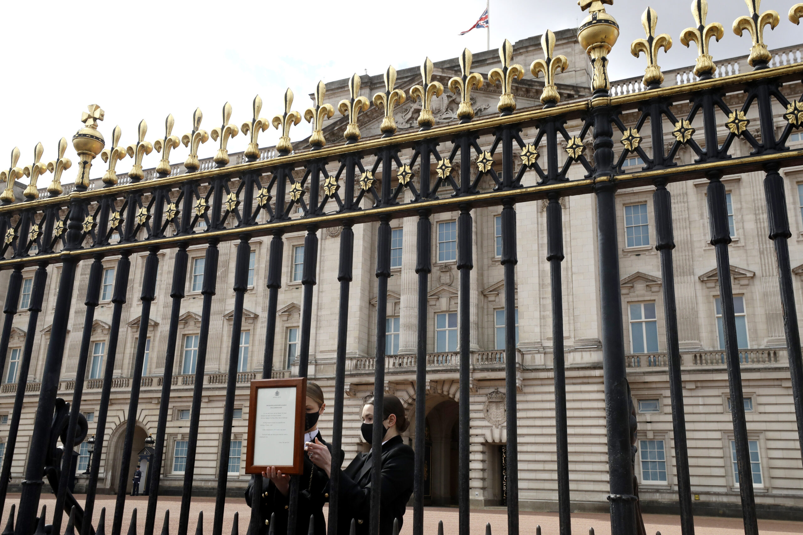 The Union flag hangs at half staff as members of staff attach an announcement, regarding the death of Britain's Prince Philip, to the fence of Buckingham Palace in London, Friday, April 9, 2021. Buckingham Palace officials say Prince Philip, the husband of Queen Elizabeth II, has died. He was 99. Philip spent a month in hospital earlier this year before being released on March 16 to return to Windsor Castle. (AP Photo/Matt Dunham)