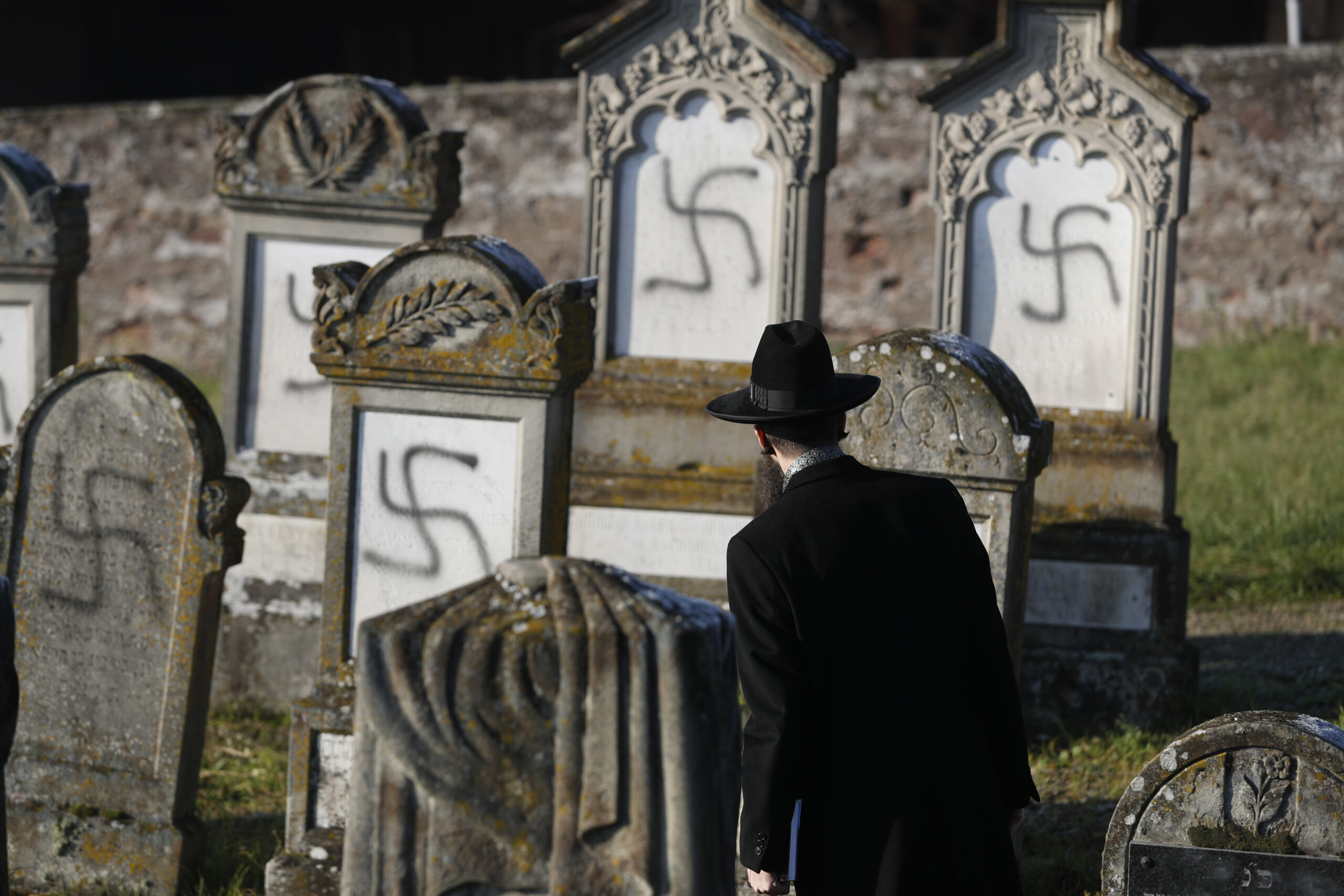 FILE - In this Dec. 4, 2019 file photo, Strasbourg chief Rabbi Harold Abraham Weill looks at vandalized tombs in the Jewish cemetery of Westhoffen, west of the city of Strasbourg, eastern France. Coronavirus lockdowns in 2020 shifted some anti-Semitic hatred online, where conspiracy theories blaming Jews for the pandemic’s medical and economic devastation abounded, Israeli researchers at Tel Aviv University's Kantor Center for the Study of Contemporary European Jewry in an annual report Wednesday, April 7, 2021. (AP Photo/Jean-Francois Badias, File)
