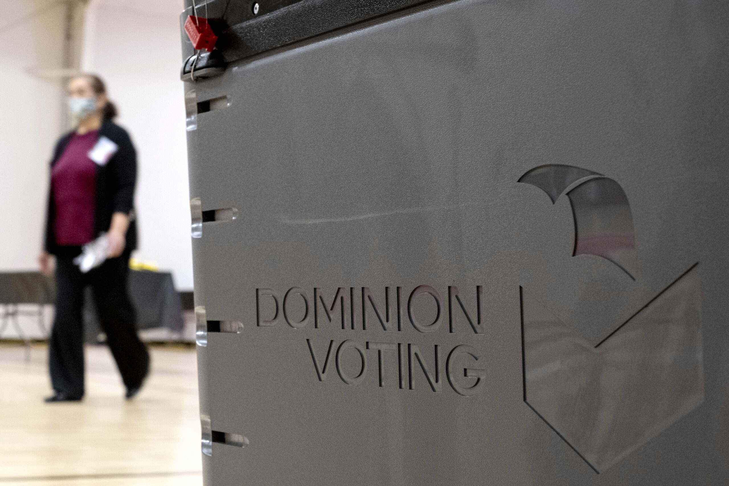 A worker passes a Dominion Voting ballot scanner while setting up a polling location at an elementary school in Gwinnett County, Ga., outside of Atlanta on Jan. 4, 2021. Newsmax has apologized to an employee of Dominion Voting Systems for airing false allegations that he manipulating voting machines or tallies on Election Day to the detriment of former President Donald Trump. Eric Coomer, security director for Dominion, subsequently dropped the conservative news network from a defamation lawsuit. (AP Photo/Ben Gray)