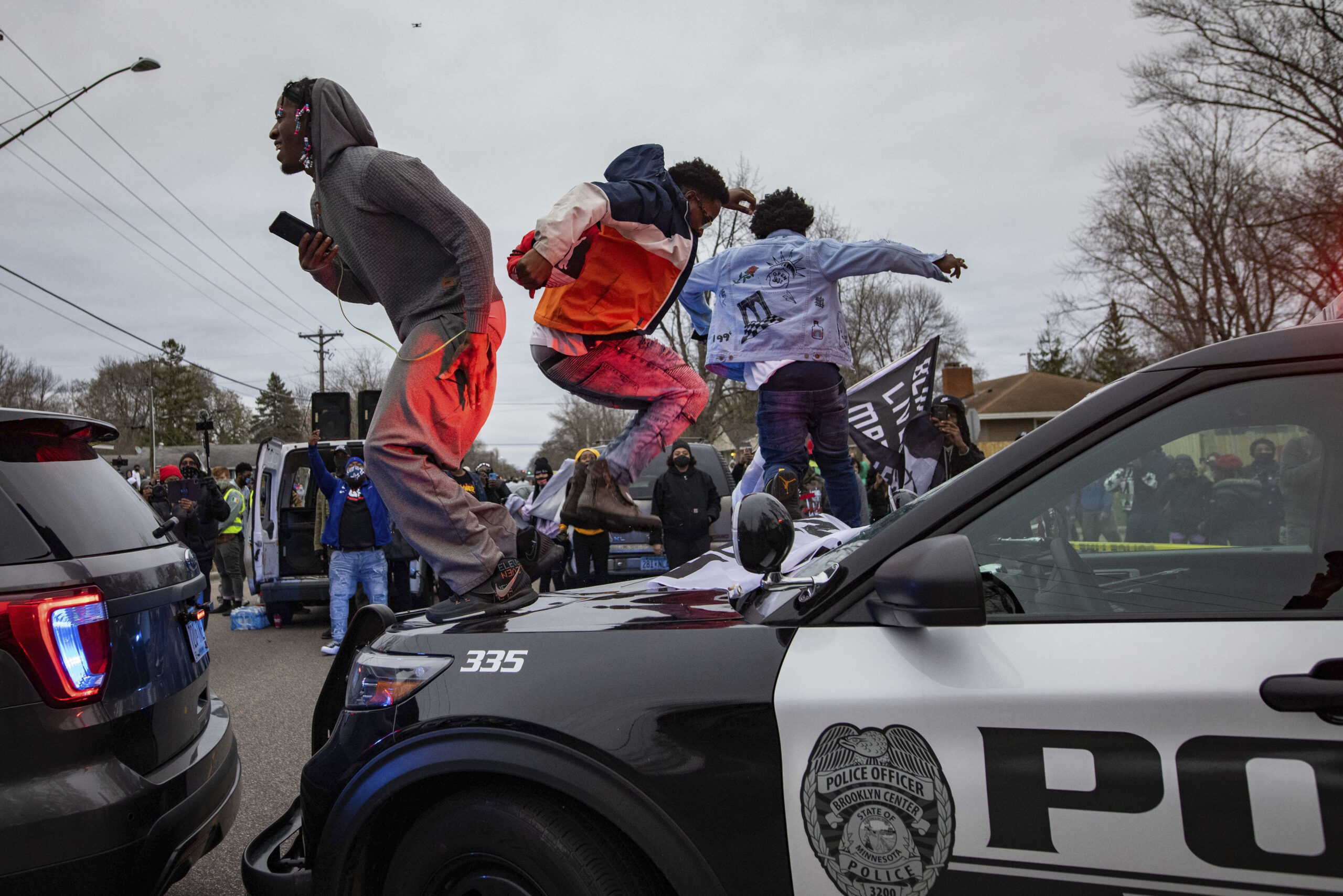 Men jump on the hood of a police car after a family said a man was shot and killed by law enforcement on Sunday, April 11, 2021, in Brooklyn Center, Minn. (AP Photo/Christian Monterrosa)