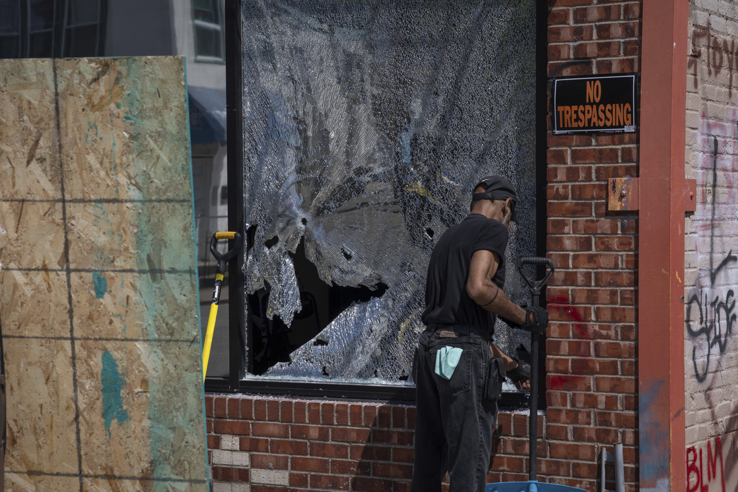 A man cleans up a broken window to a barber shop after shots were fired in George Floyd Square on the one year anniversary of George Floyd's death on Tuesday, May 25, 2021, in Minneapolis. The intersection where George Floyd died was disrupted by gunfire Tuesday, just hours before it was to be the site of a family-friendly street festival marking the anniversary of his death at the hands of police.(AP Photo/Christian Monterrosa)