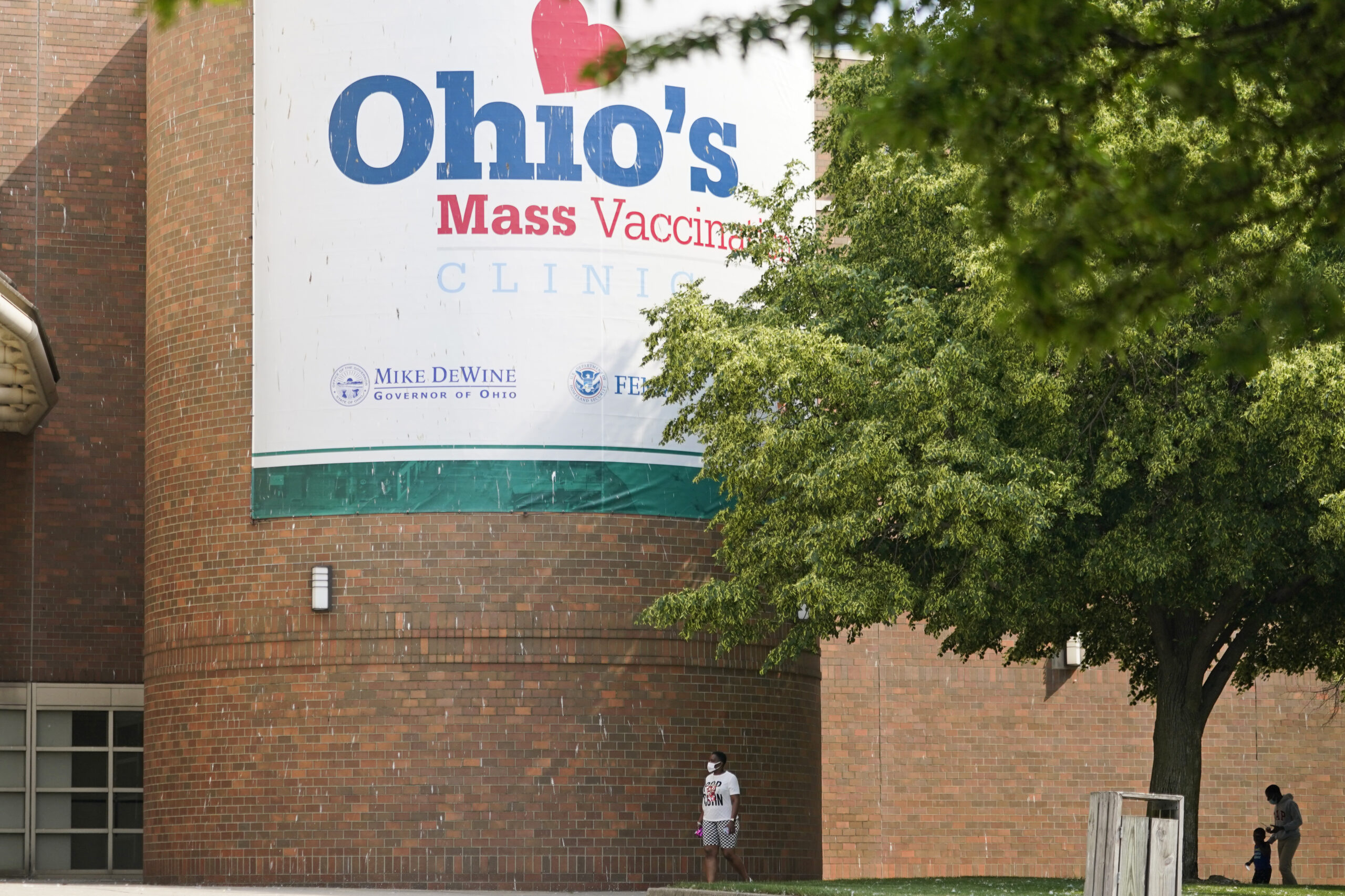 People walk past sign displayed for Ohio's COVID-19 mass vaccination clinic at Cleveland State University, Tuesday, May 25, 2021, in Cleveland. Nearly 2.8 million residents have registered for Ohio's Vax-a-Million vaccination incentive program, with participants hoping to win either the $1 million prize for adults or a full-ride college scholarship for children, Gov. Mike DeWine announced Monday, May 24. The winners will be announced Wednesday night at the end of the Ohio Lottery's Cash Explosion TV show, and then each Wednesday for the next four weeks. (AP Photo/Tony Dejak)