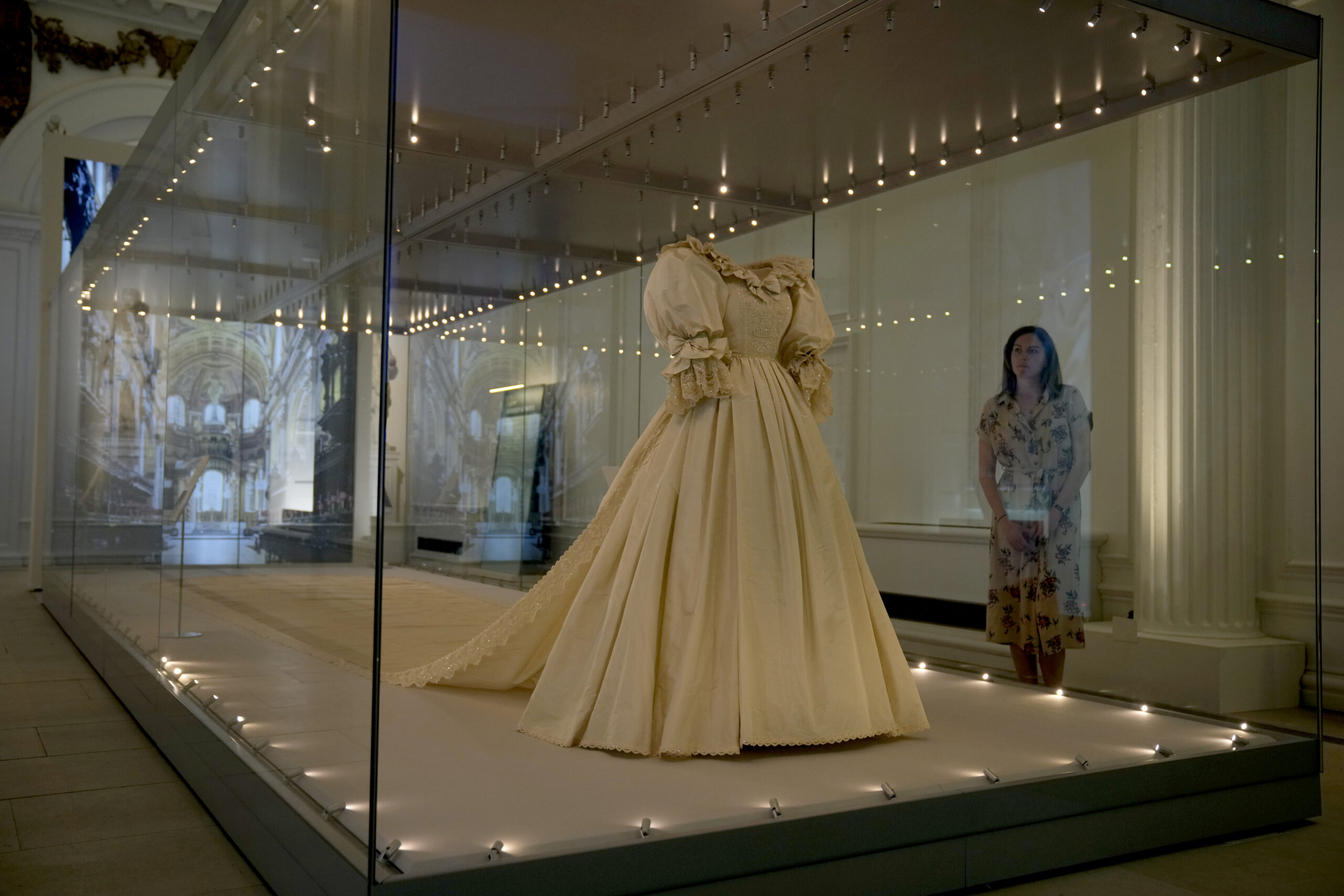 A staff member poses for photographers next to the wedding dress of Britain's Princess Diana during a media preview for the "Royal Style in the Making" exhibition at Kensington Palace in London, Wednesday June 2, 2021. The exhibition, which opens to visitors on Thursday and runs until January 2, 2022, explores the intimate relationship between fashion designer and royal client. (AP Photo/Matt Dunham)