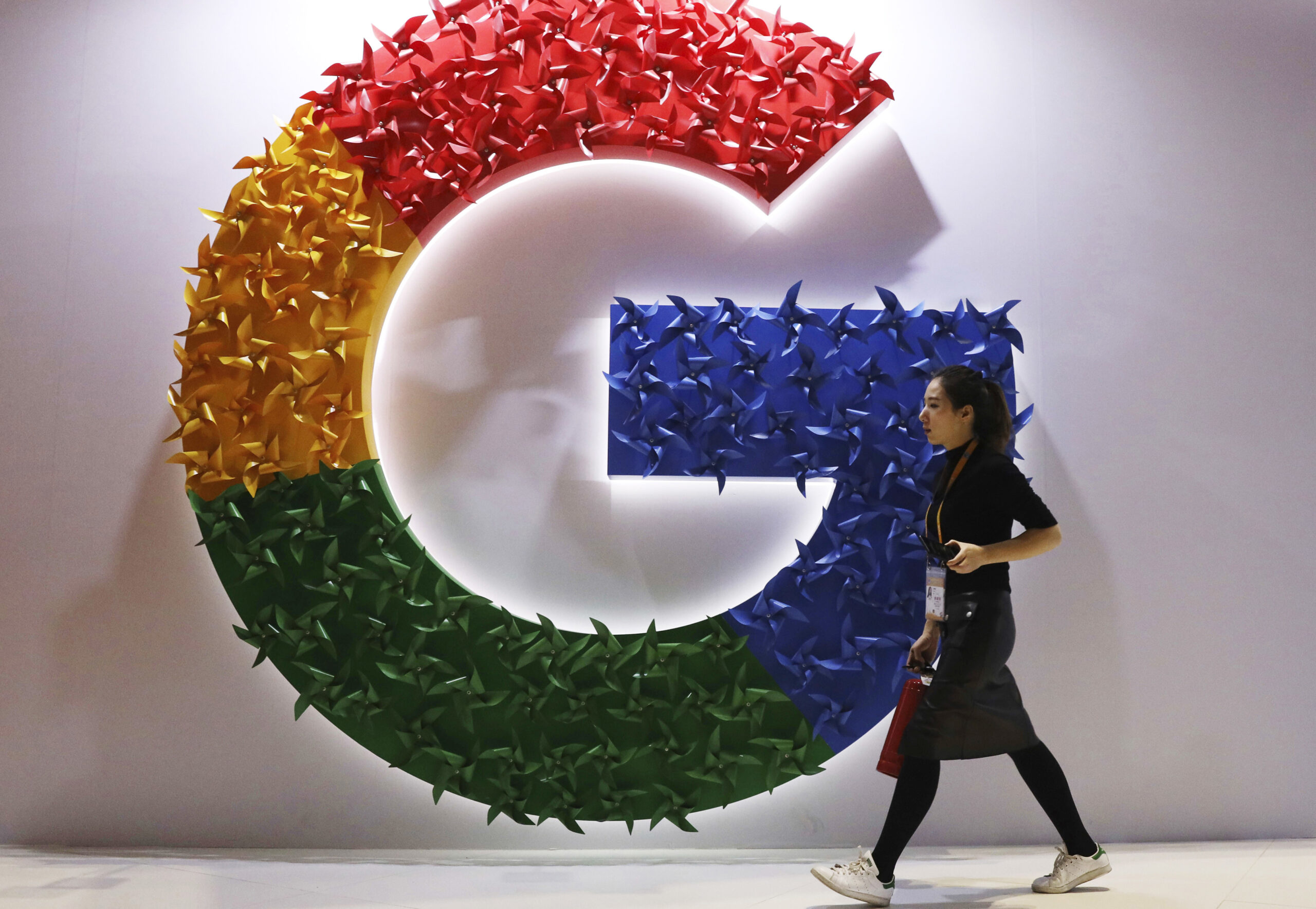 FILE - In this Monday, Nov. 5, 2018 file photo, a woman walks past the logo for Google at the China International Import Expo in Shanghai. France's anti-competition watchdog has decided to fine Google 220 million euros ($268 million) for abusing its “dominant position” in the complex business of online advertising. It said Monday, June 7, 2021 that the move is unprecedented. (AP Photo/Ng Han Guan, File)