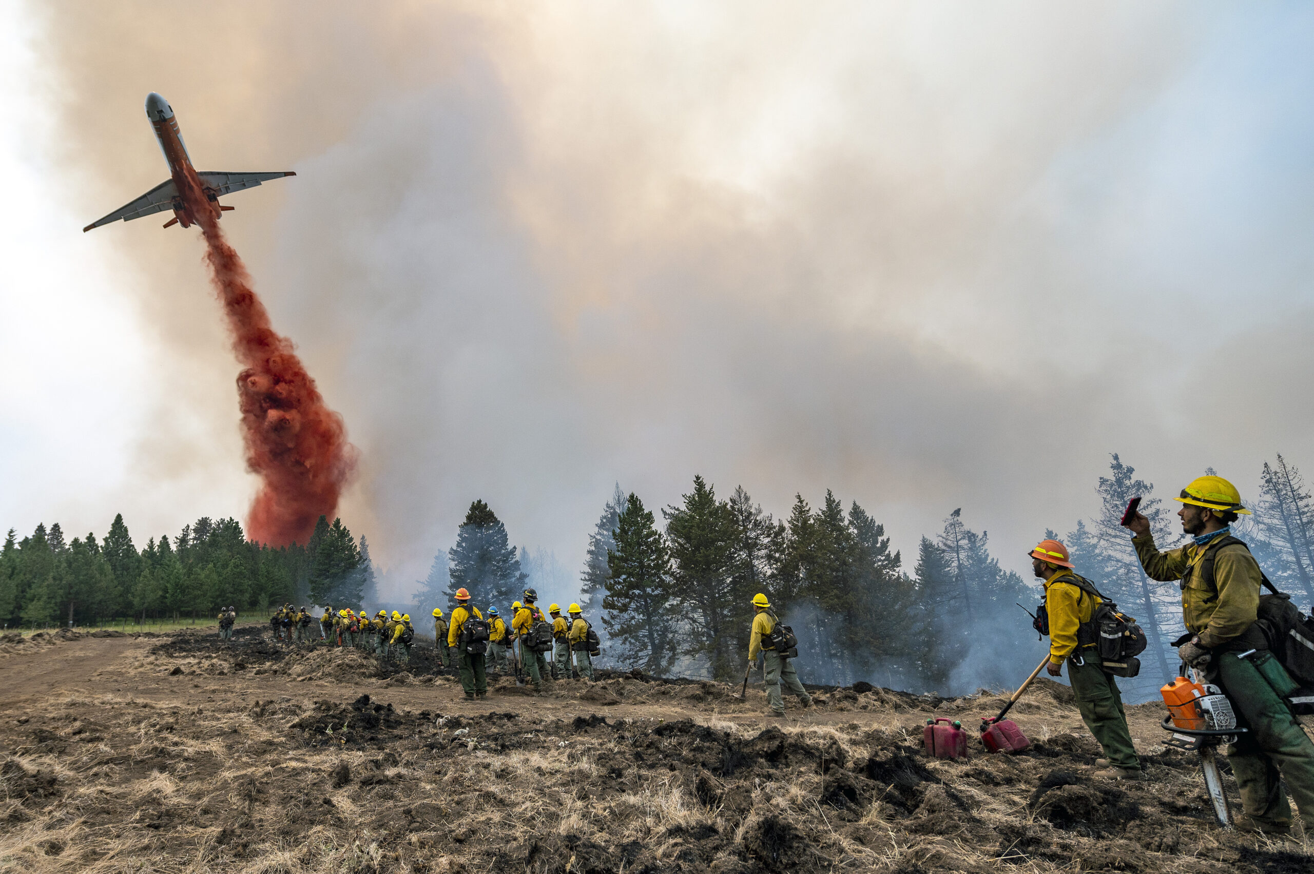 Wildland firefighters watch and take video with their cellphones as a plane drops fire retardant on Harlow Ridge above the Lick Creek Fire, southwest of Asotin, Wash., Monday, July 12, 2021. The fire, which started last Wednesday, has now burned over 50,000 acres of land between Asotin County and Garfield County in southeast Washington state. (Pete Caster/Lewiston Tribune via AP)