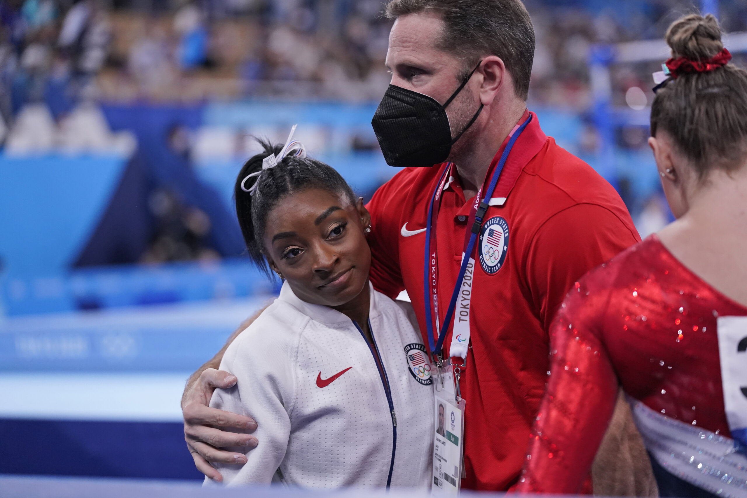 Coach Laurent Landi embraces Simone Biles, after she exited the team final with apparent injury, at the 2020 Summer Olympics, Tuesday, July 27, 2021, in Tokyo. The 24-year-old reigning Olympic gymnastics champion Biles huddled with a trainer after landing her vault. She then exited the competition floor with the team doctor. (AP Photo/Gregory Bull)
