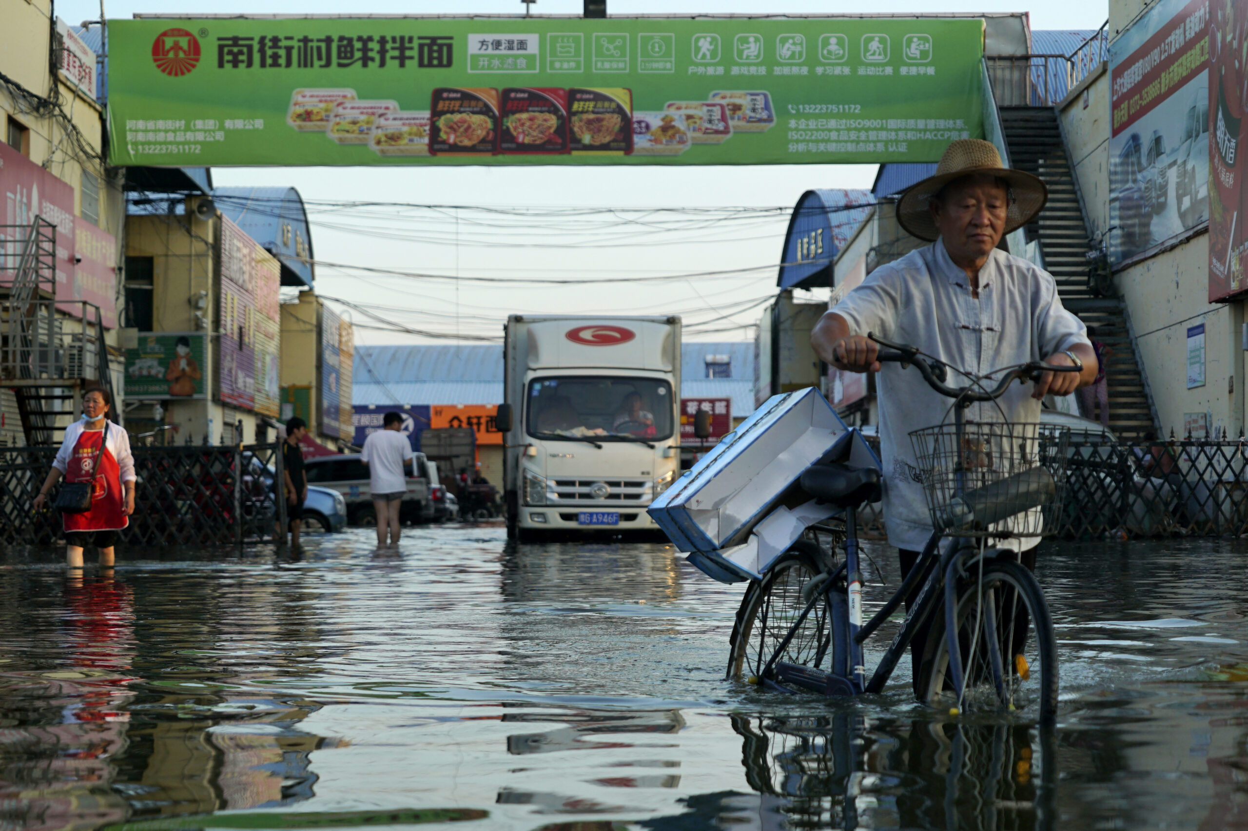FILE - In this Monday, July 26, 2021 file photo, a man carries goods on his bicycle as he walks out of the the Yubei Agricultural and Aquatic Products World in Xinxiang in central China's Henan Province. The Intergovernmental Panel on Climate Change report released on Monday, Aug. 9, 2021, says warming already is smacking Earth hard and quickly with accelerating sea level rise, shrinking ice and worsening extremes such as heat waves, droughts, floods and storms. (AP Photo/Dake Kang, File)