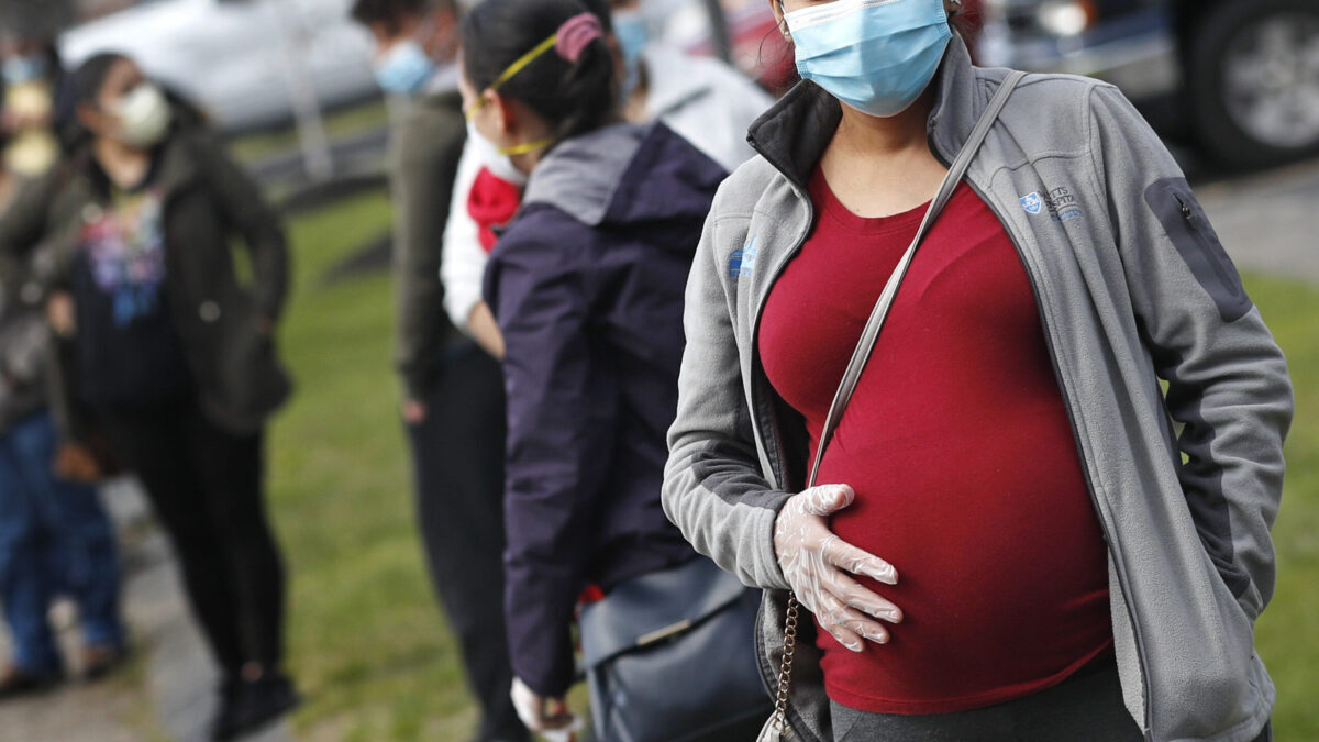 FILE - In this May 7, 2020 file photo, a pregnant woman wearing a face mask and gloves holds her belly as she waits in line for groceries at St. Mary's Church in Waltham, Mass. The Centers for Disease Control and Prevention urged all pregnant women Wednesday, Aug. 11, 2021 to get the COVID-19 vaccine as hospitals in hot spots around the U.S. see disturbingly high numbers of unvaccinated mothers-to-be seriously ill with the virus. (AP Photo/Charles Krupa, file)