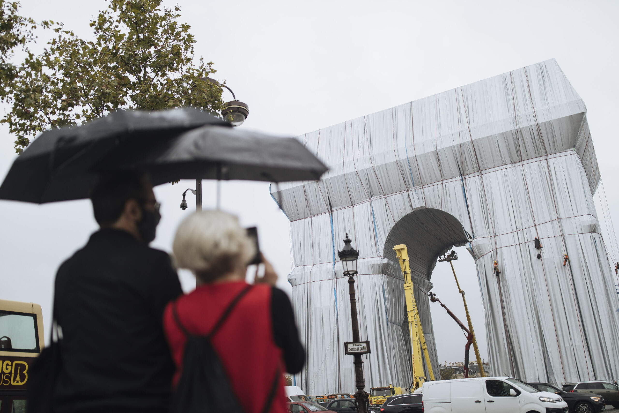 People watch workers wrapping the Arc de Triomphe monument, Wednesday, Sept. 15, 2021 in Paris. The "L'Arc de Triomphe, Wrapped" project by late artist Christo and Jeanne-Claude will be on view from, Sept. 18 to Oct. 3. The famed Paris monument will be wrapped in 25,000 square meters of fabric in silvery blue, and with 3,000 meters of red rope. (AP Photo/Lewis Joly)
