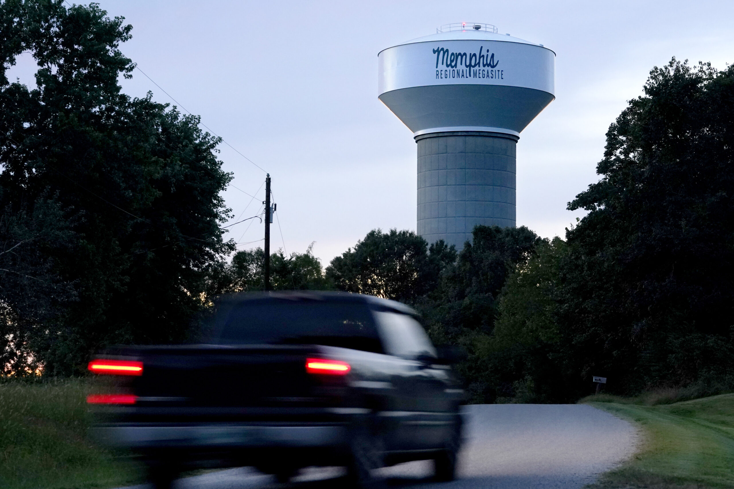 A truck drives down a rural road near a water tower marking the location of the Memphis Regional Megasite on Sept. 24, 2021, in Stanton, Tenn. Ford Motor Co. and SK Innovation of South Korea plan to build three new electric-vehicle battery factories and an auto assembly plant by 2025 in Tennessee and Kentucky. The industrial site in Stanton will be the location for a factory to produce electric F-Series pickups and a battery factory. (AP Photo/Mark Humphrey)