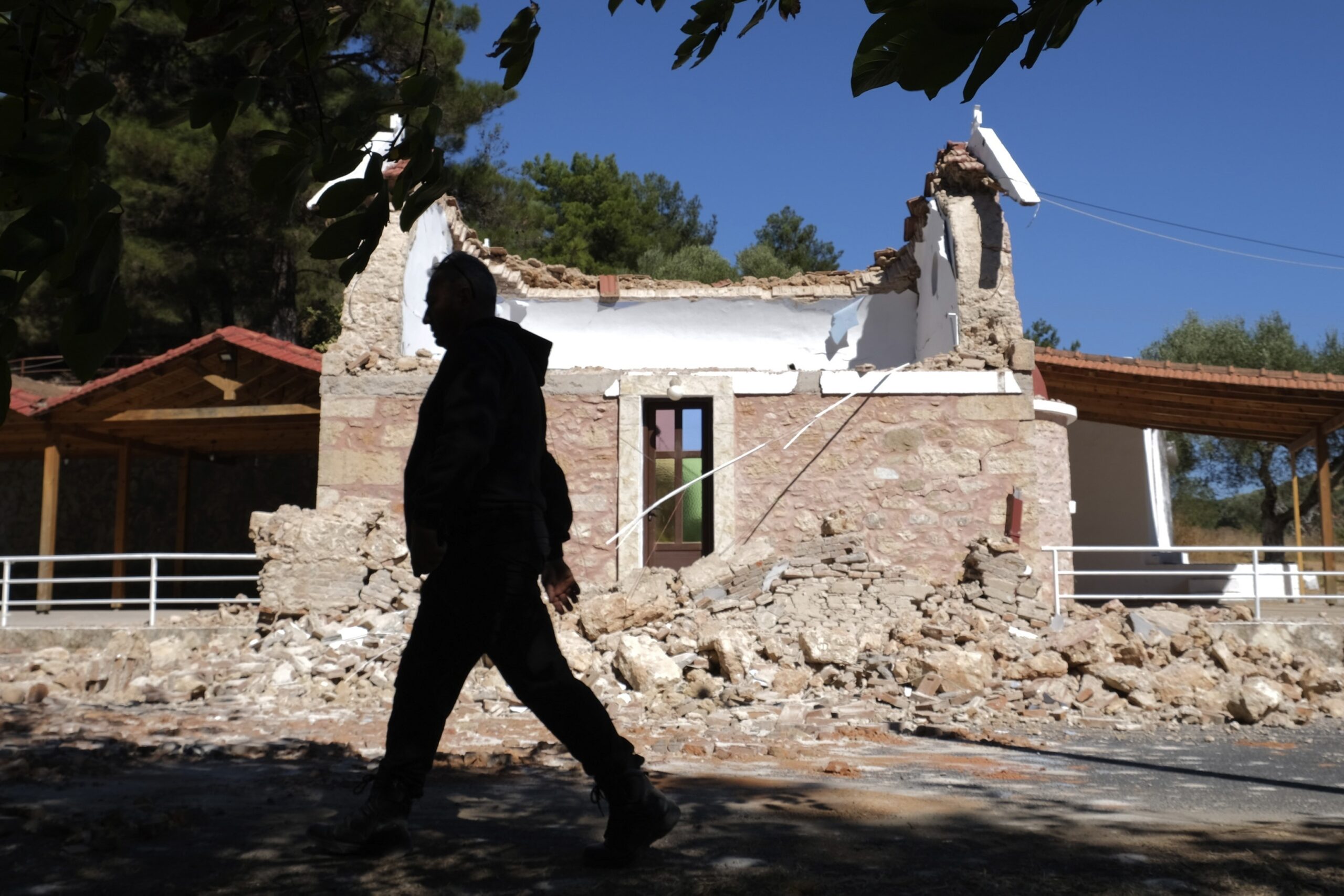 A Resident passes next to a damaged Greek Orthodox chapel after a strong earthquake in Arcalochori village on the southern island of Crete, Greece, Monday, Sept. 27, 2021. A strong earthquake with a preliminary magnitude of 5.8 has struck the southern Greek island of Crete, and Greek authorities say one person has been killed and several more have been injured. (AP Photo/Harry Nikos)