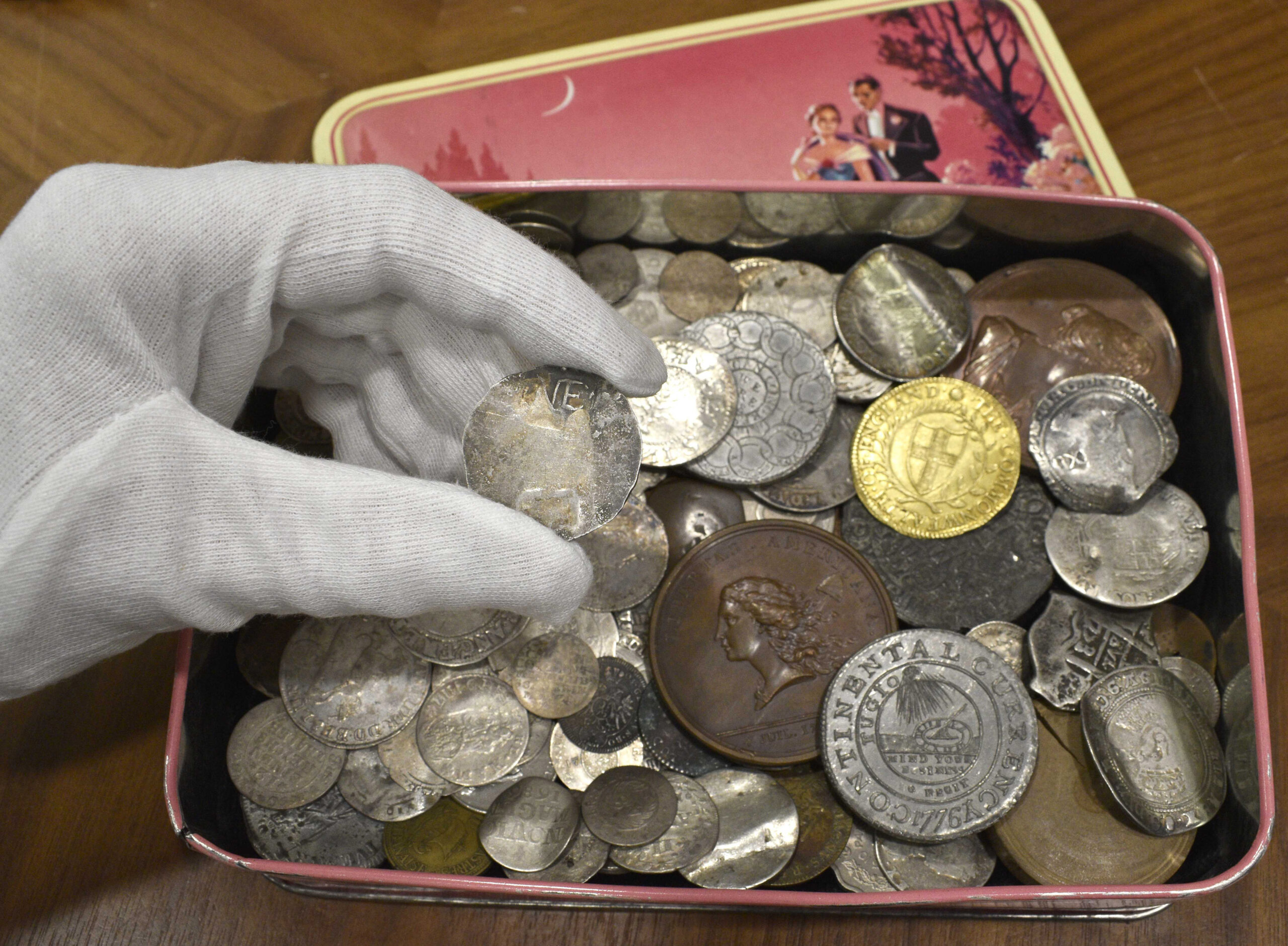 In this Sept. 9, 2021 photo provided by auctioneer Morton & Eden Ltd., a rare 17th century one shilling coin is displayed above a metal box containing other coins, at the auction house, in London. Morton & Eden Ltd. says the extraordinarily rare coin, with a face value of just pennies when it was minted in mid-17th century New England, could sell for the equivalent of about $300,000 when it's put up for auction in London next month. (Menelaos Danellis/Morton & Eden Ltd. via AP)