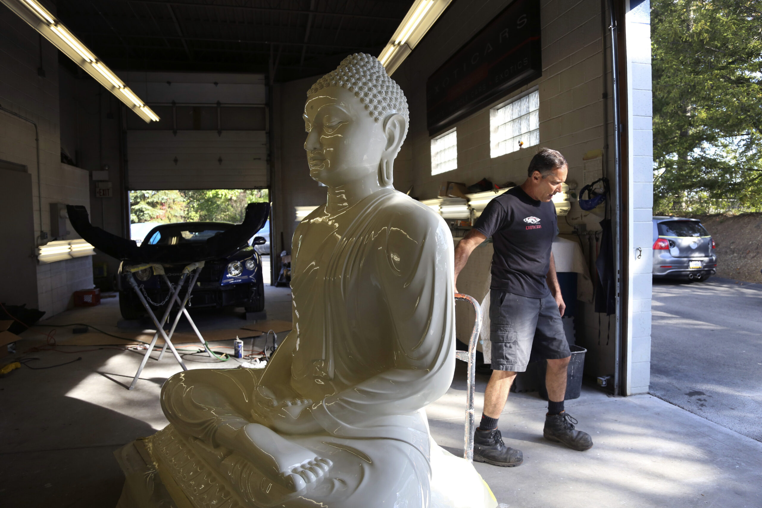 Dave Ley, co-owner of Exoticars, an auto restoration shop specializing in classic vehicles, pulls a restored statue of the Buddha outside in McCandless, Pa., on Monday, Oct. 11, 2021. Workers repaired and repainted the figure for the Pittsburgh Buddhist Center, which brought it from Sri Lanka over 15 years ago. (AP Photo/Jessie Wardarski)