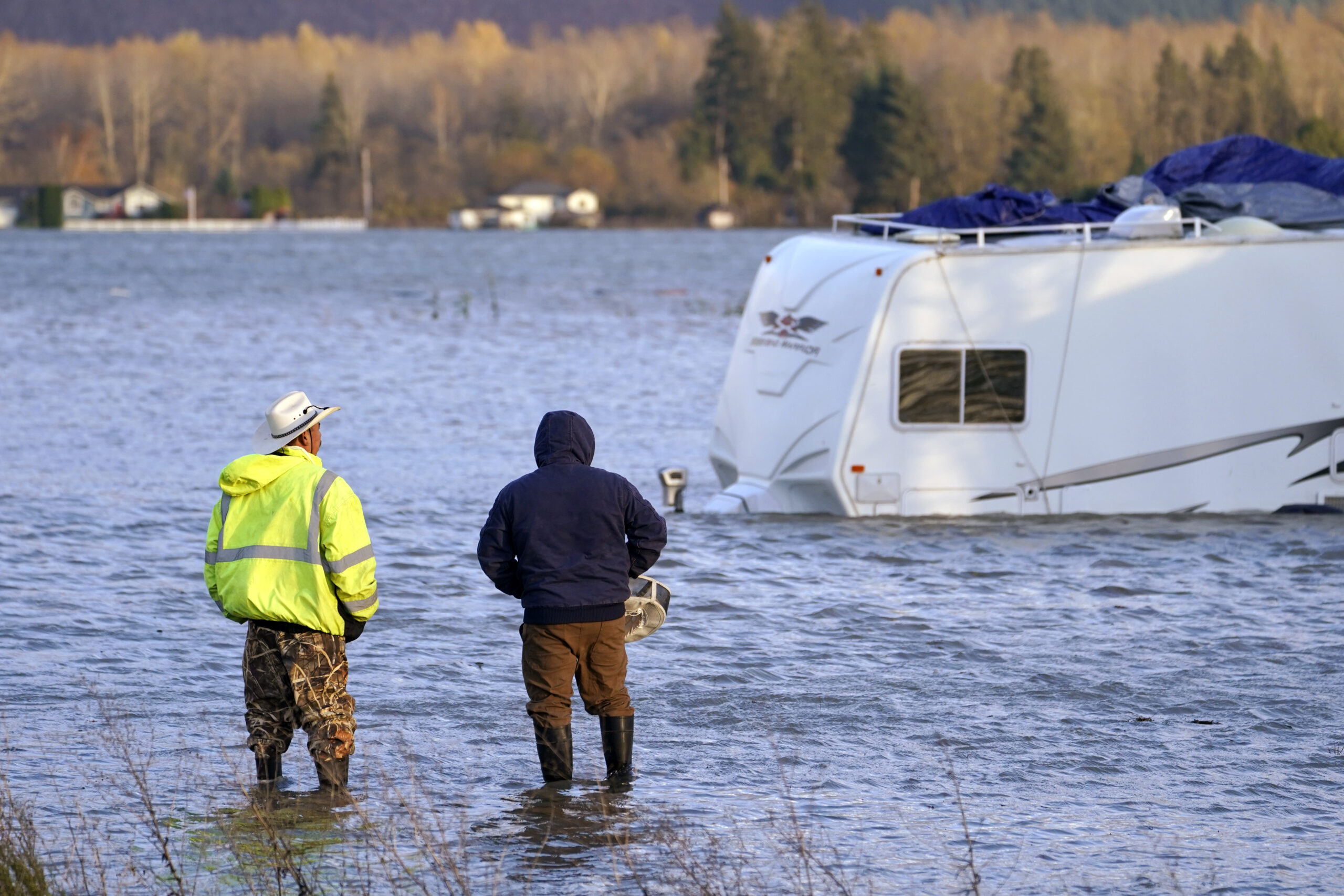 Two men stand in the flooded Skagit River and look across at an RV, Monday, Nov. 15, 2021, in Sedro-Woolley, Wash. (AP Photo/Elaine Thompson)