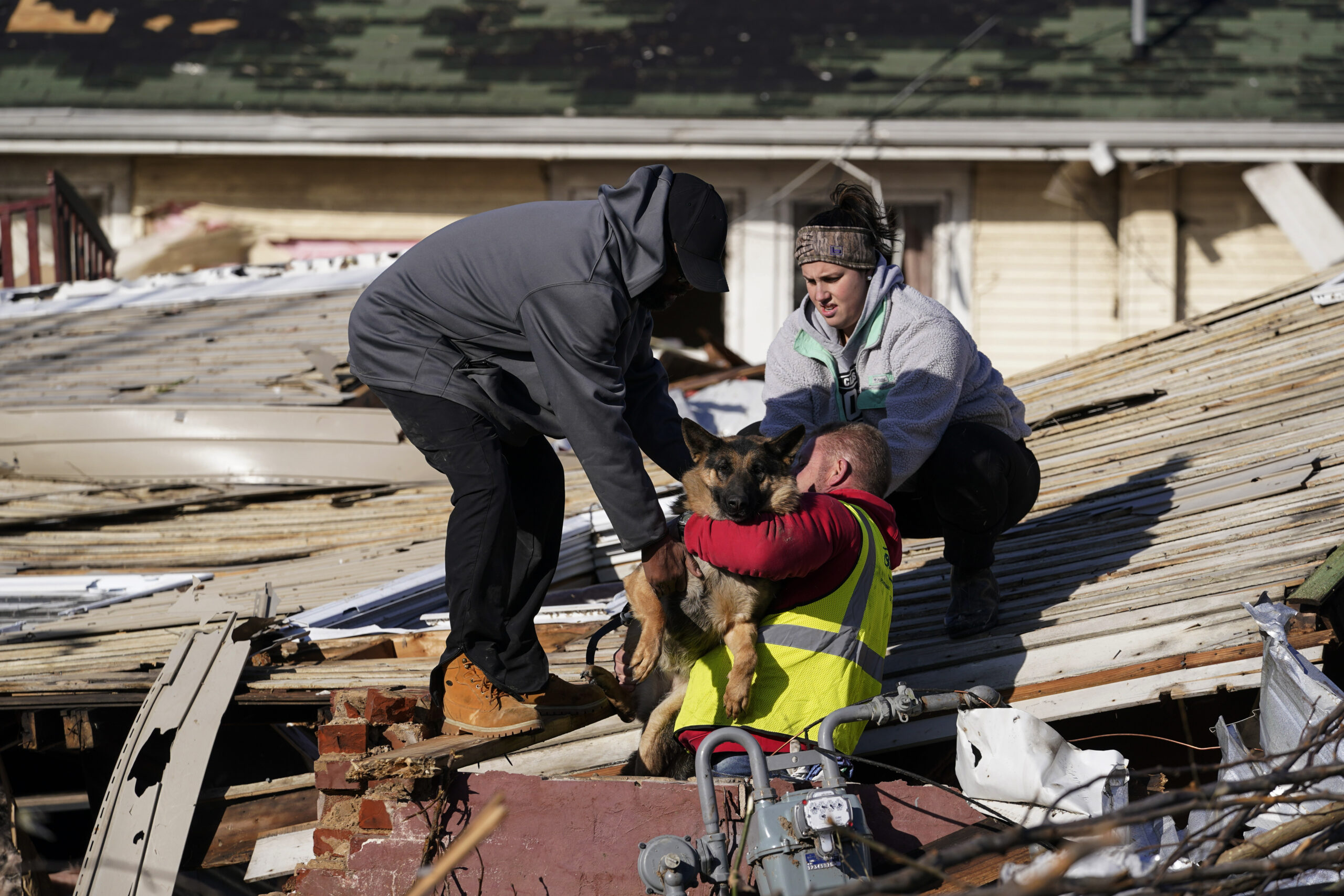 Dog owner Derrick Starks, left, Chris Buchanan, center and Niki Thompson, right, both from neighboring counties, attempt to rescue Cheyenne from a tornado-damaged home in Mayfield, Ky., on Saturday, Dec. 11, 2021. Tornadoes and severe weather caused catastrophic damage across multiple states late Friday, killing dozens of people overnight. (AP Photo/Mark Humphrey)