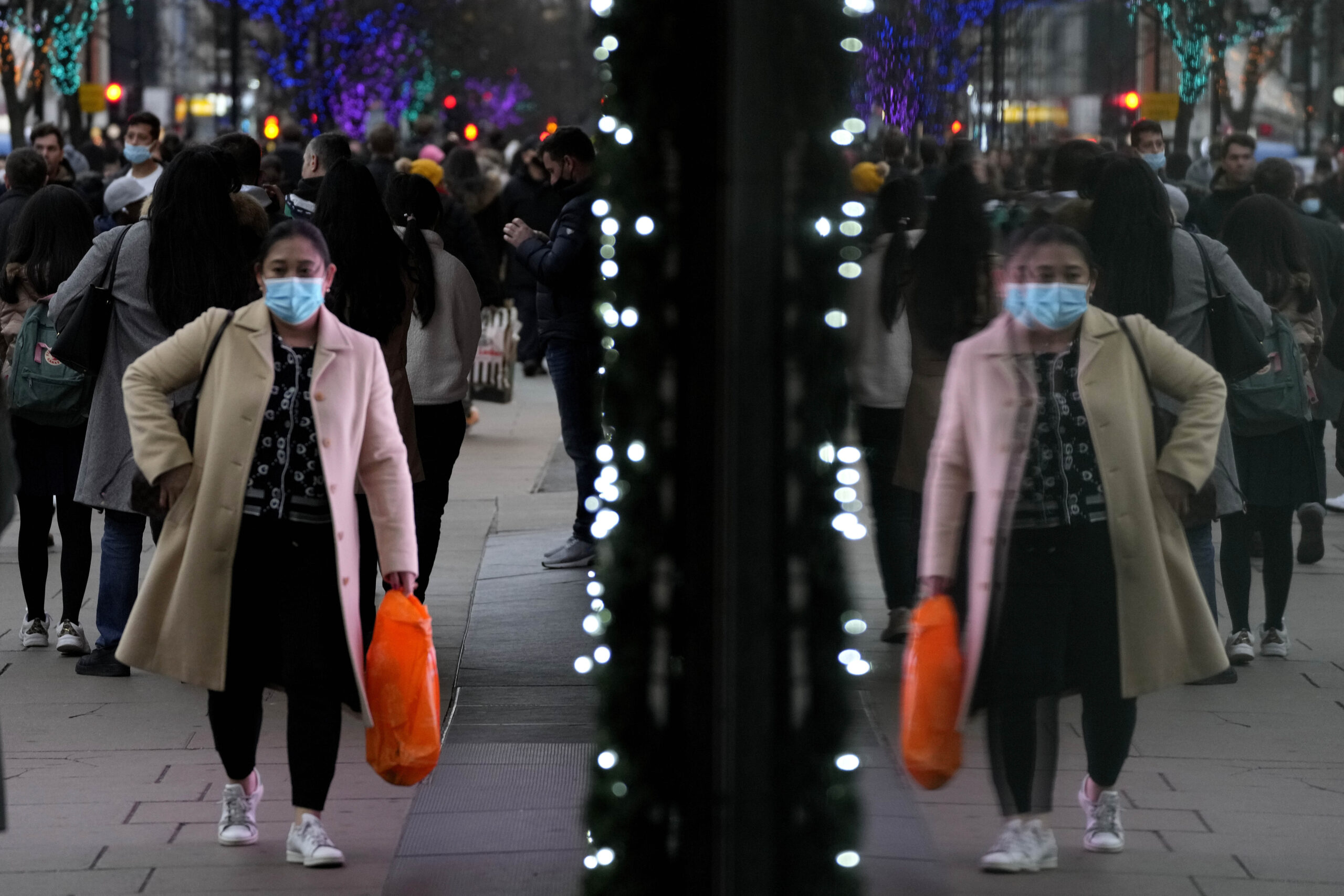 Shoppers are reflected in a window as they walk down Oxford Street, Europe's busiest shopping street, in London, Thursday, Dec. 23, 2021. (AP Photo/Frank Augstein)