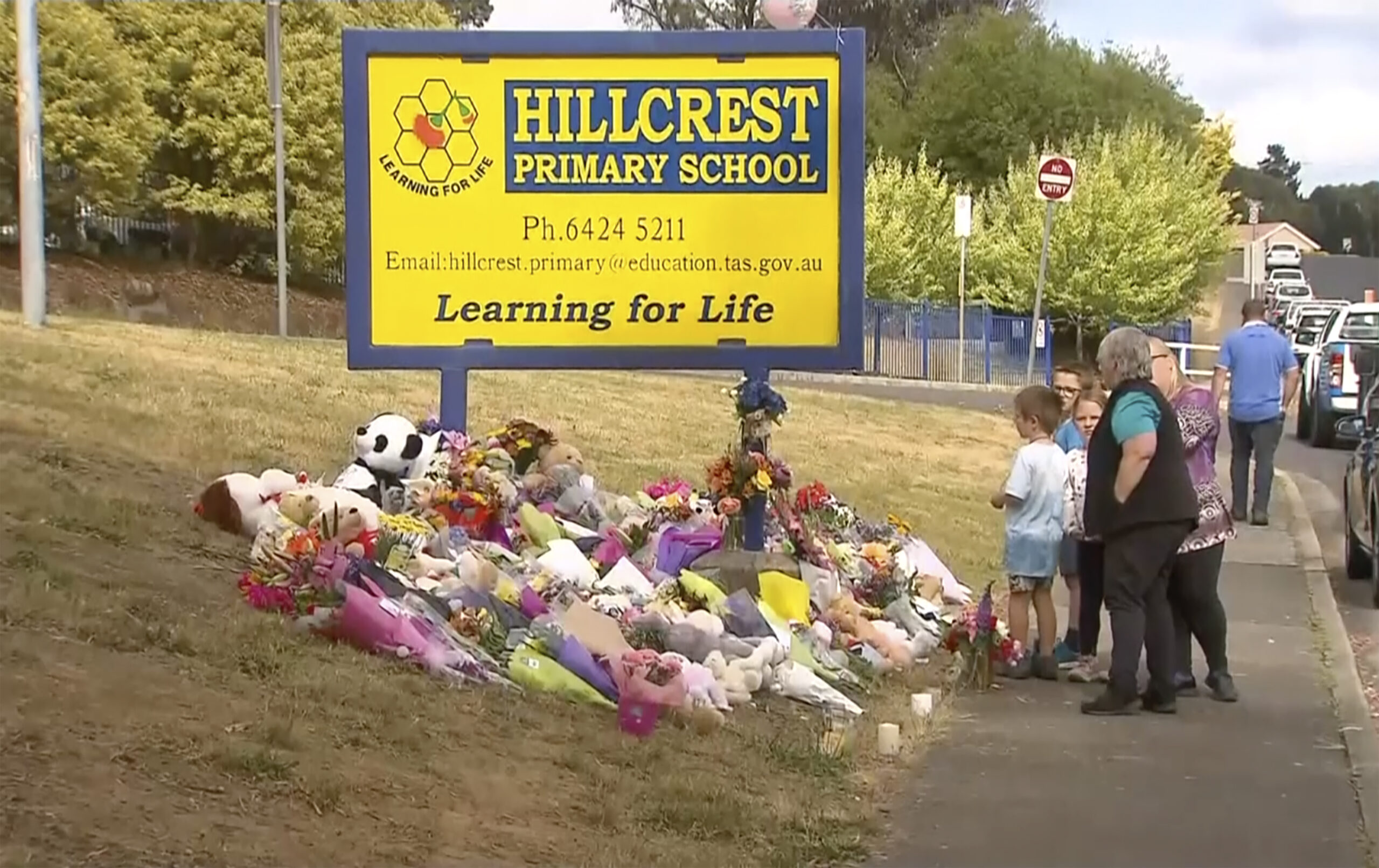 In this image made from video, people lay flowers at a makeshift memorial outside the Hillcrest Primary School in Devonport, Tasmania, Australia, Friday, Dec. 17, 2021. Local residents on Friday placed floral tributes outside the Australian school where five children died after falling from a bouncy castle that was lifted into the air by a gust of wind. (Channel 9 via AP)
