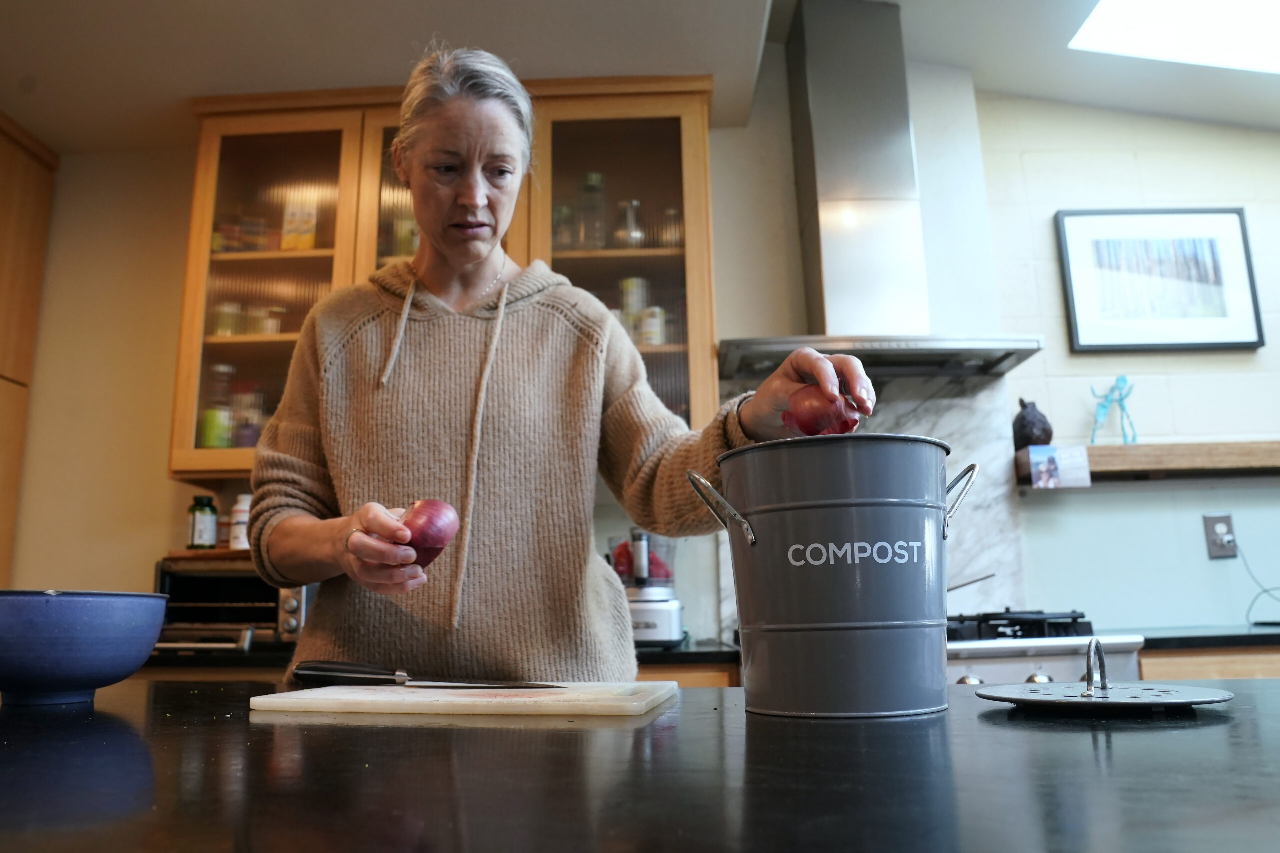 Joy Klineberg tosses an onion peel into container to be used for composting while preparing a family meal at her home in Davis, Calif., Tuesday, Nov. 30, 2021. In January 2022, new rules take effect in California requiring people to recycle their food waste to be combusted or turned into energy. Davis already requires residents to recycle their food waste into the yard waste bin instead of the trash. (AP Photo/Rich Pedroncelli)