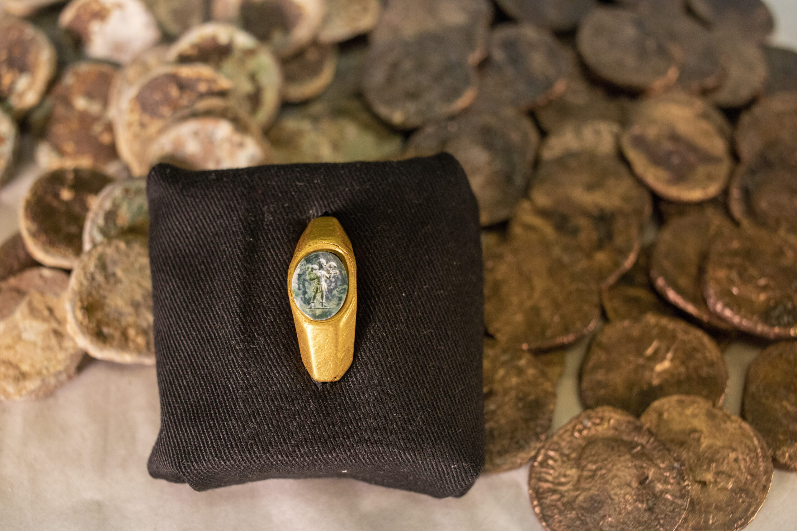 Roman gold ring, its green gemstone carved with the figure of a shepherd carrying a sheep on his shoulders is on display with coins that where found near the ancient city of Caesarea, dated to the Roman and Mamluk periods, around 1,700 and 600 years ago, in Jerusalem, Wednesday, Dec. 22, 2021. The Israel Antiquities Authority says it discovered the remnants of two shipwrecks off the Mediterranean coast replete with a sunken trove of hundreds of silver and bronze coins and Roman and medieval artifacts. "The image, of the 'Good Shepherd', is one of the earliest and oldest images used in Christianity for symbolizing Jesus," the IAA said in its announcement, speculating that the owner may have been an early Christian. (AP Photo/Ariel Schalit)