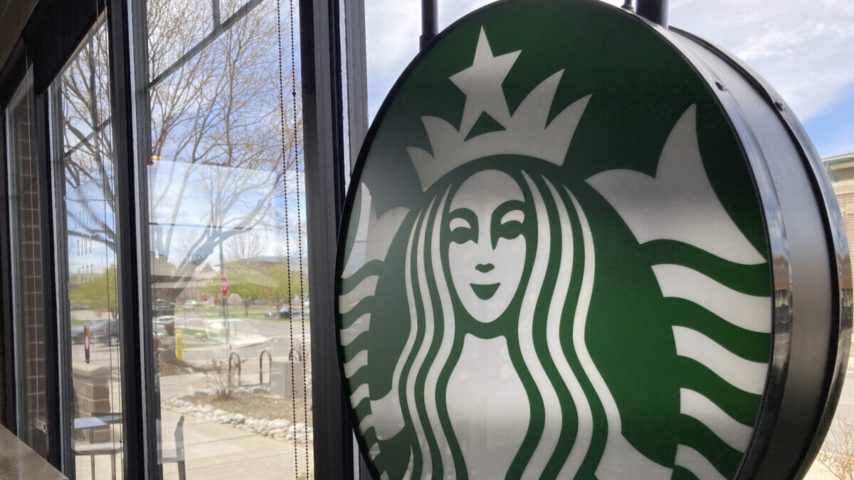 A sign bearing the corporate logo hangs in the window of a Starbucks open only to take-away customers in this photograph taken Monday, April 26, 2021, in southeast Denver. Starbucks is no longer requiring its U.S. workers to be vaccinated against COVID-19, reversing a policy it announced earlier this month. The Seattle coffee giant says, Wednesday, Jan. 19, 2022, it's responding to last week’s ruling by the U.S. Supreme Court. (AP Photo/David Zalubowski)