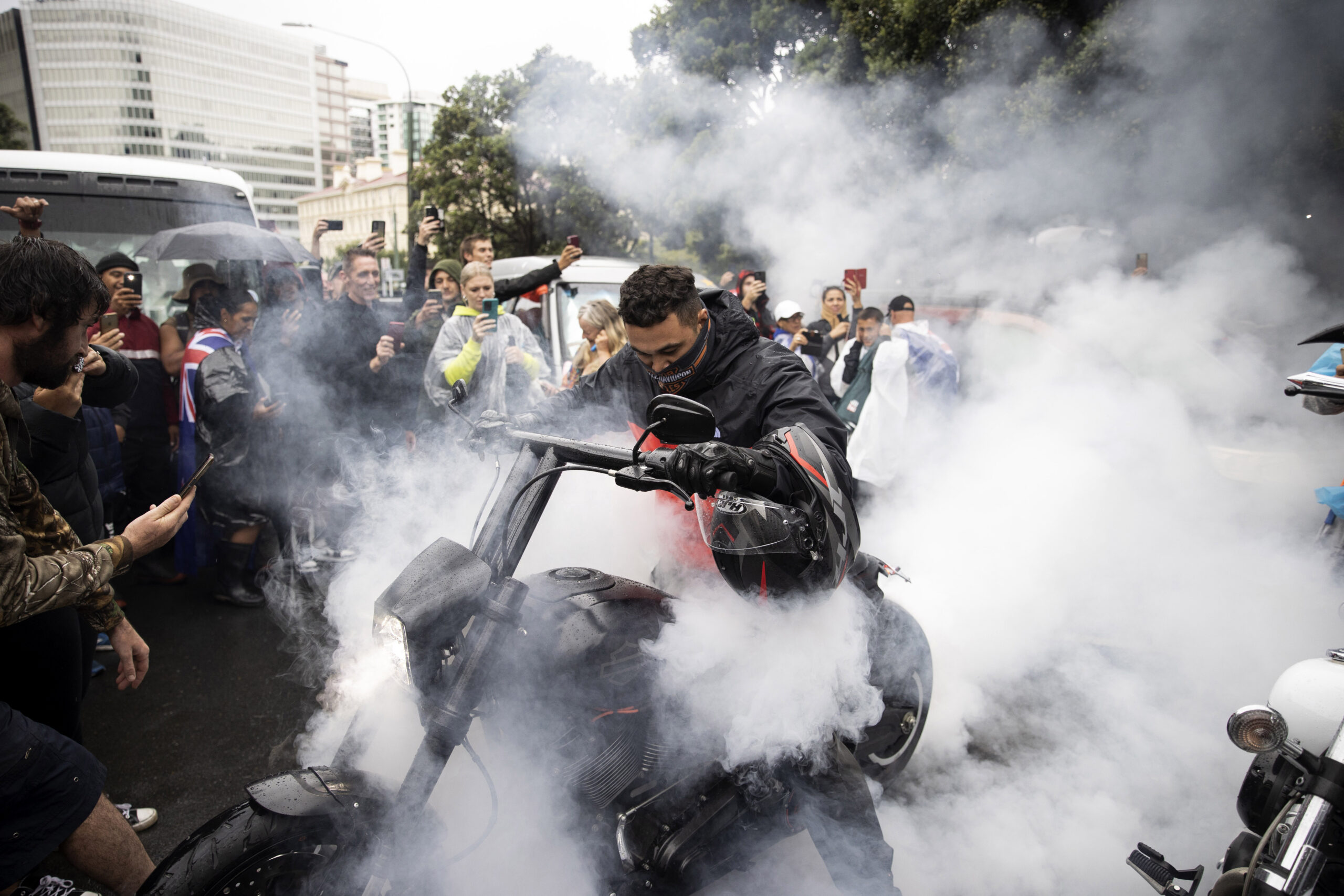 Protesters watch as a man spins the tire on his motorcycle in wet conditions as they demonstrate their opposition to coronavirus vaccine mandates at Parliament in Wellington, New Zealand, Saturday, Feb. 12, 2022. The protest began when a convoy of trucks and cars drove to Parliament from around the nation, inspired by protests in Canada. (George Heard/NZME via AP)
