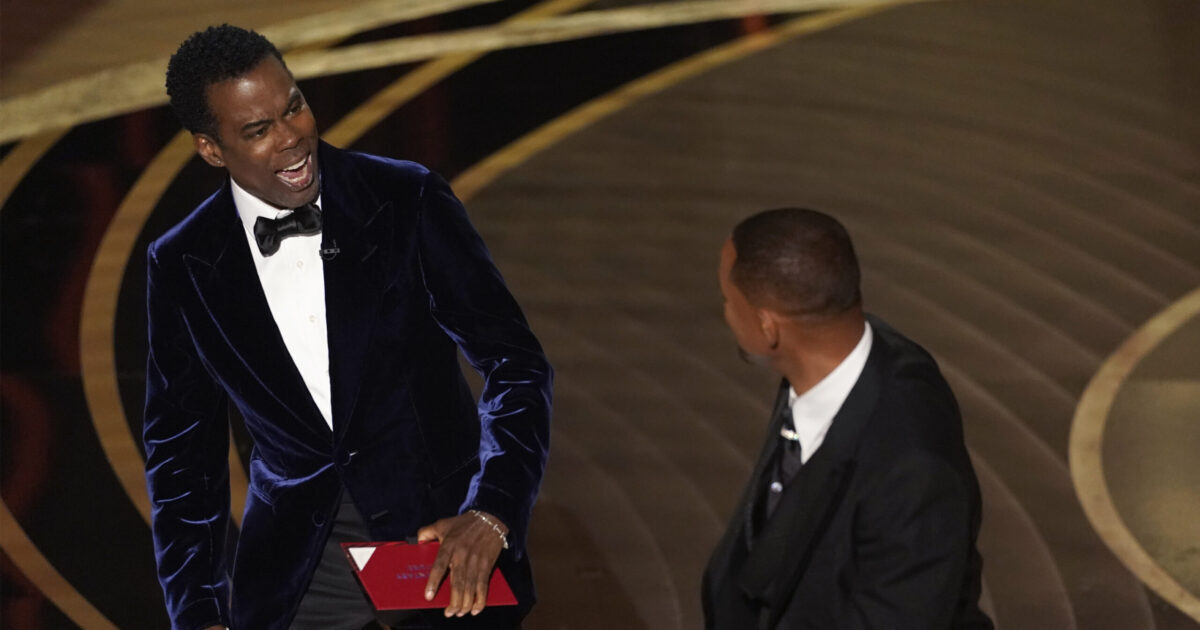 presenter Chris Rock, left, reacts after being hit on stage by Will Smith while presenting the award for best documentary feature at the Oscars on Sunday, March 27, 2022, at the Dolby Theatre in Los Angeles. (AP Photo/Chris Pizzello)