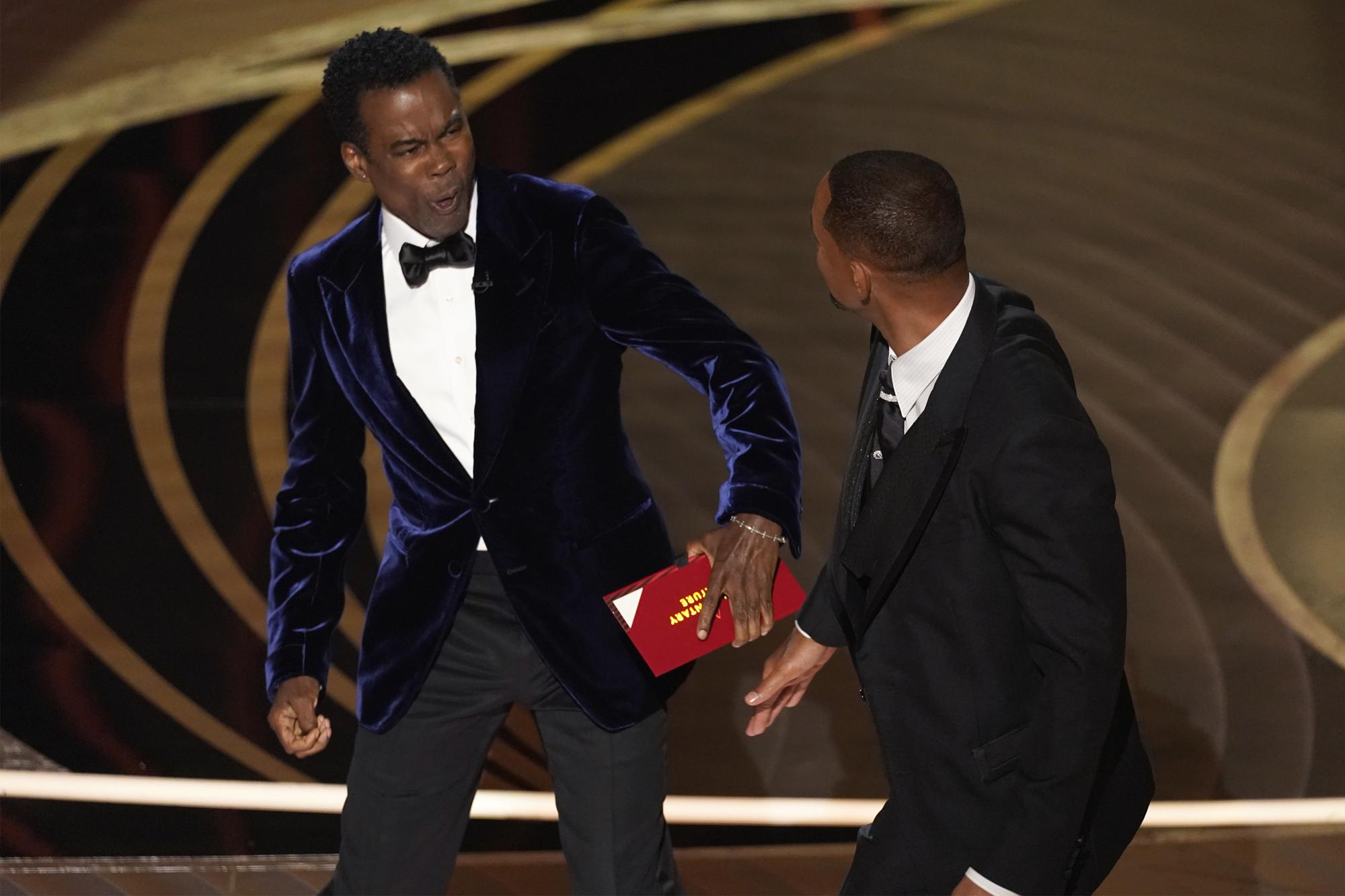 Presenter Chris Rock, left, reacts after being hit on stage by Will Smith while presenting the award for best documentary feature at the Oscars on Sunday, March 27, 2022, at the Dolby Theatre in Los Angeles. 