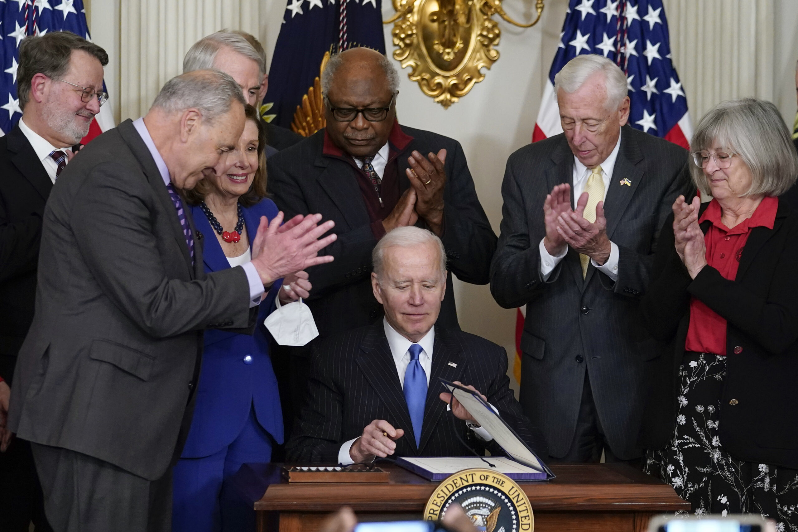 President Joe Biden signs the Postal Service Reform Act of 2022 in the State Dining Room at the White House in Washington, Wednesday, April 6, 2022. Watching from left are Sen. Gary Peters, D-Mich., Senate Majority Leader Chuck Schumer of N.Y., Sen. Rob Portman, R-Ohio, House Speaker Nancy Pelosi of Calif., Rep. James Clyburn, D-S.C., Rep. Steny Hoyer, D-Md., and Annette Taylor. (AP Photo/Susan Walsh)