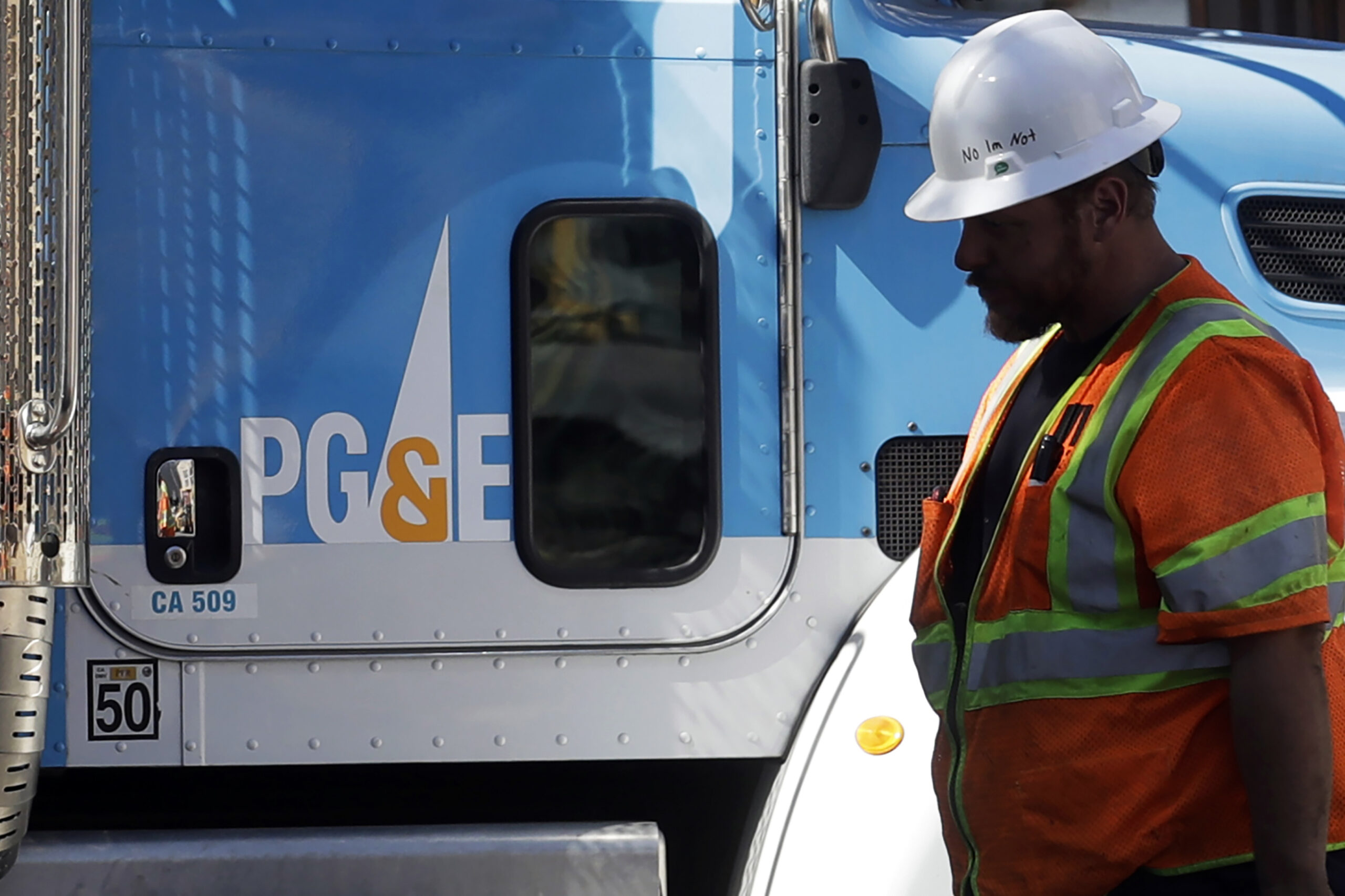 FILE - In this Aug. 15, 2019, file photo, a Pacific Gas & Electric worker walks in front of a truck in San Francisco. Pacific Gas & Electric has agreed to pay more than $55 million to avoid criminal prosecution for two major wildfires started by its aging equipment in 2019 and 2021, prosecutors announced. (AP Photo/Jeff Chiu, File)