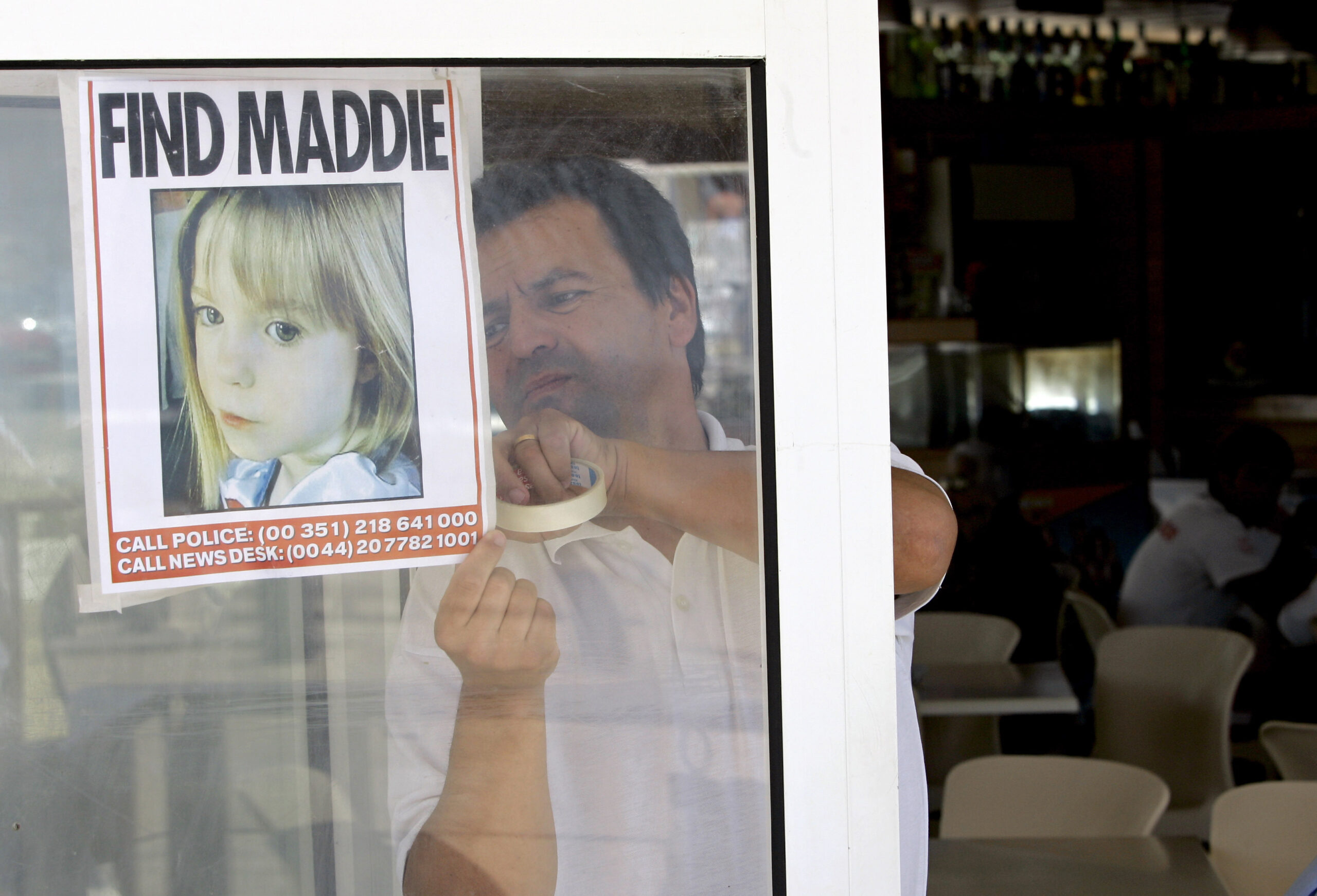 FILE - A waiter hangs a picture of missing 3-year-old girl Madeleine McCann on a restaurant's window, Thursday, May 10 2007, in Praia da Luz, southern Portugal. Prosecutors in southern Portugal are formally accusing a suspect in the investigation into the disappearance of Madeleine McCann, a British girl who disappeared nearly 15 years ago while on a family vacation in the southern European country. A statement on Thursday, April 21, 2022, by the Public Ministry district of Faro, the largest city in Portugal's Algarve region, did not name the suspect but said they were acting on a request by German authorities and in coordination with English investigators. (AP Photo/Armando Franca, File)