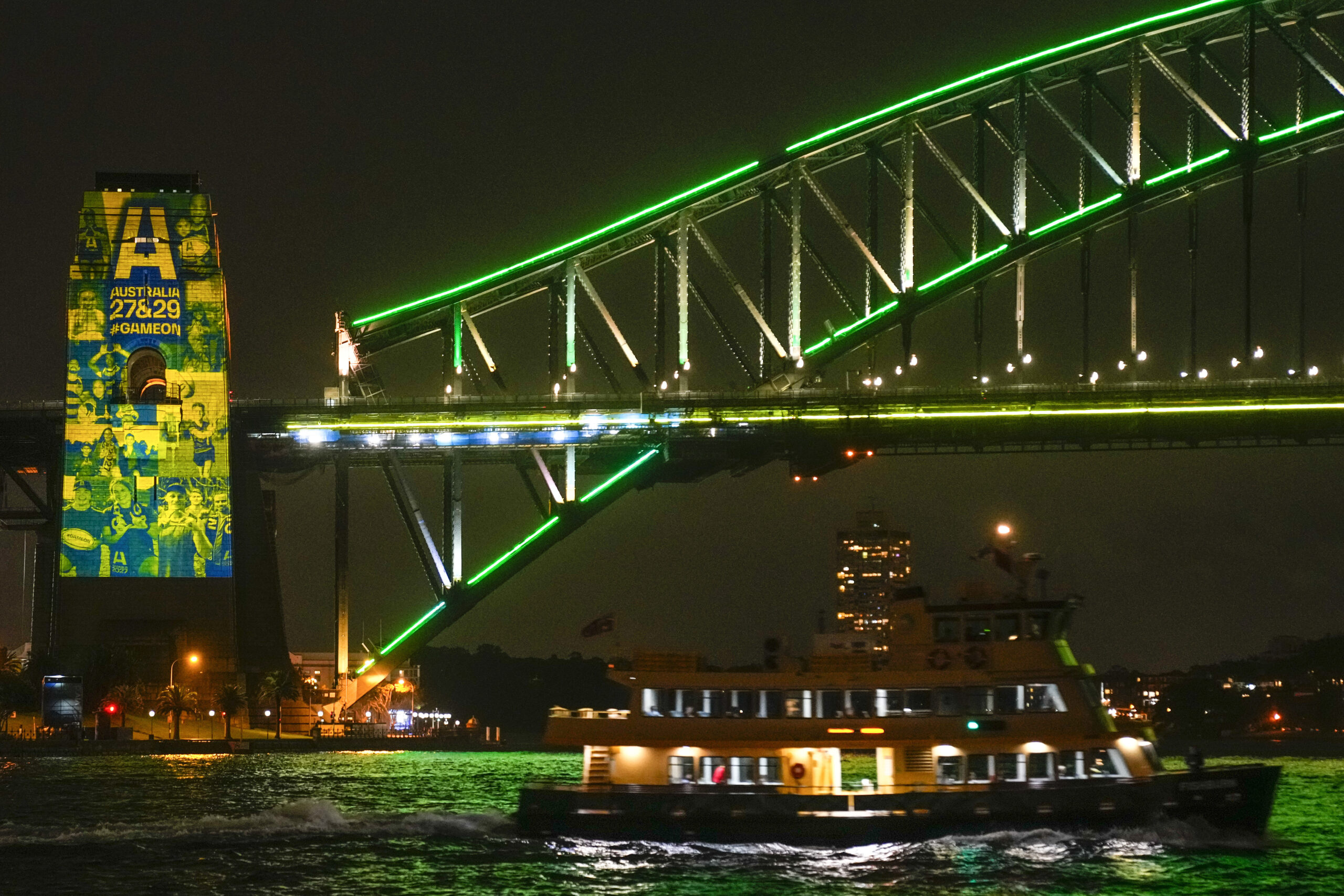 A Sydney ferry sails past the illuminated pylon of the Sydney Harbour Bridge ahead of the final vote for the hosting of the Rugby World Cups, Thursday, May 12, 2022. World Rugby will announce the host nations for the men's and women's World Cups for the period 2025-2033 with Australia heavily favored to host the men's 2027 and women's tournaments in 2029. (AP Photo/Mark Baker)