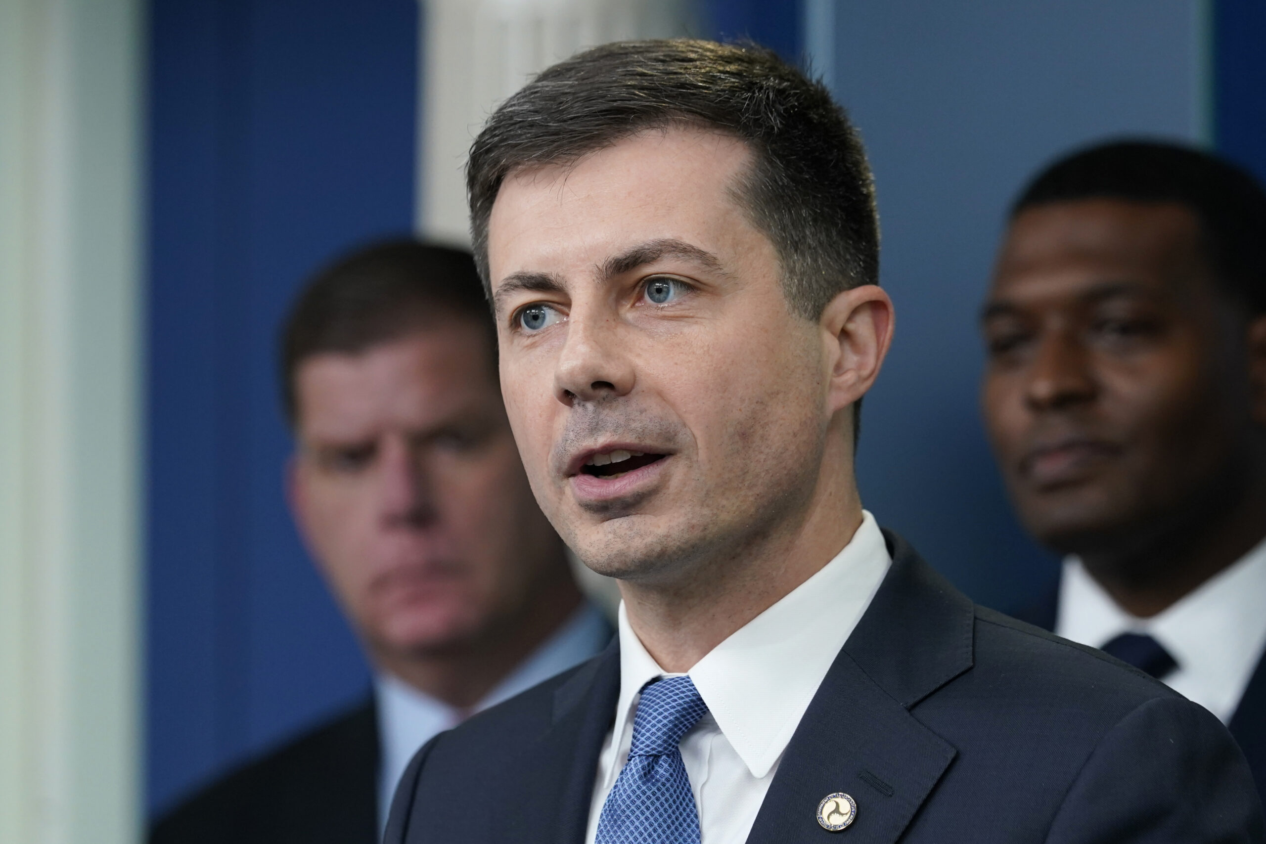 FILE - Transportation Secretary Pete Buttigieg, center, speaks during a briefing at the White House in Washington, May 16, 2022, as Labor Secretary Marty Walsh, left, and Environmental Protection Agency administrator Michael Regan, right, listen. Buttigieg says he is pushing airlines to hire more customer-service people and take other steps to help travelers this summer. (AP Photo/Susan Walsh, File)